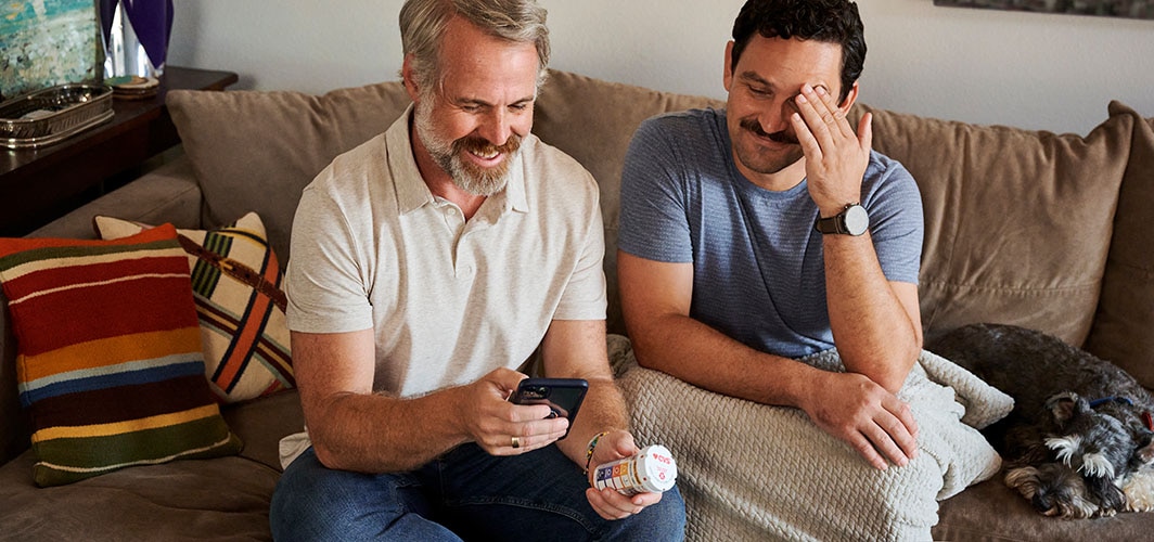 Two men sitting on a couch looking at a cell phone