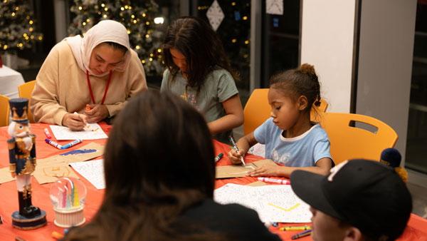 Several children seated around a table working on a hands-on art activity with paper, markers, and craft supplies during a community event.