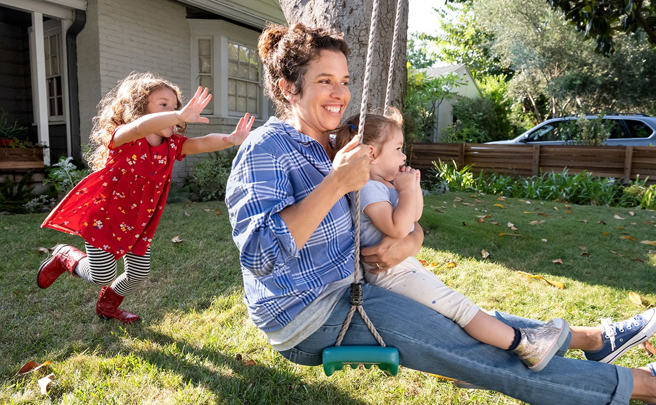 A woman on a swing set with her two young daughters