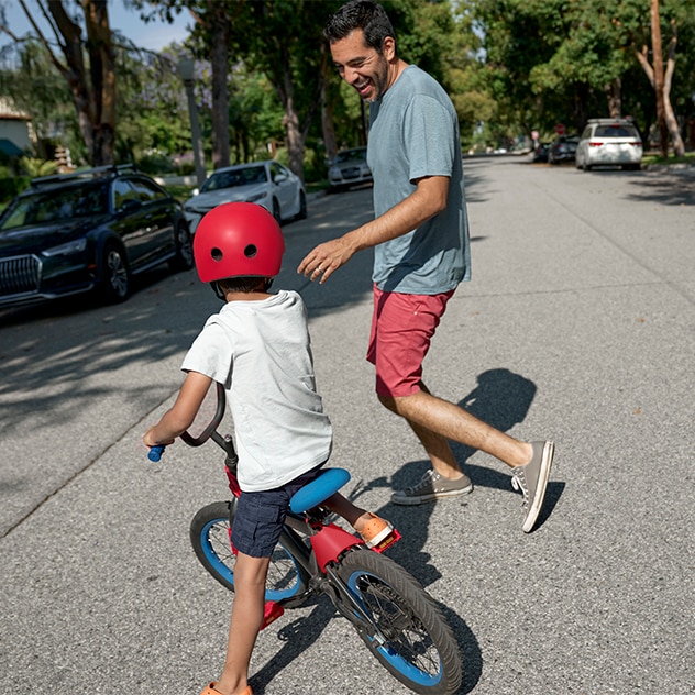 Young boy rides bicycle while father watches him