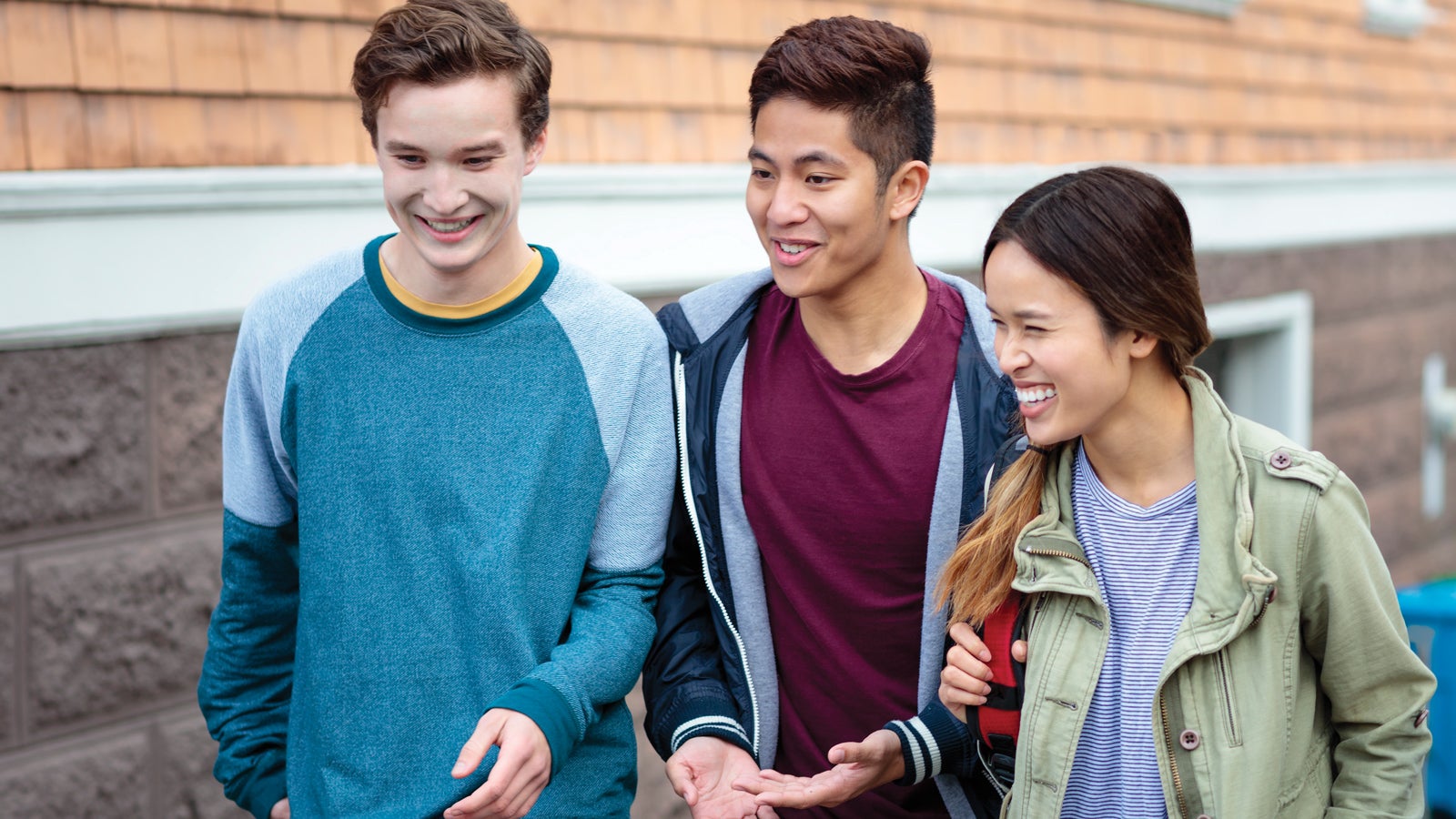 Three millennial friends smile as they walk together.