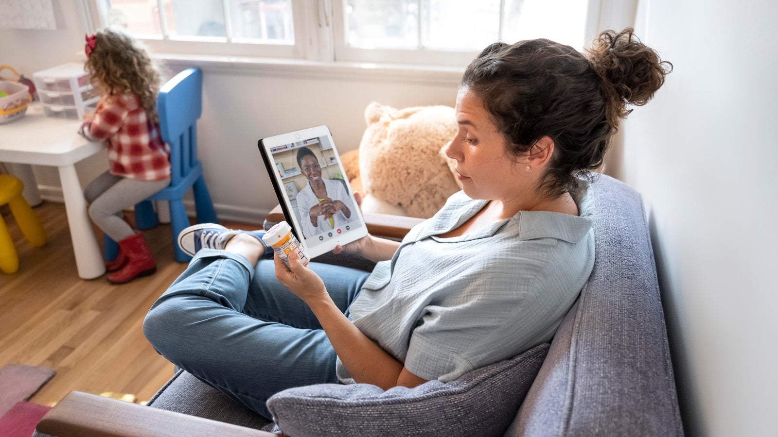 A patient has a telehealth call with a healthcare provider while watching her daughter.