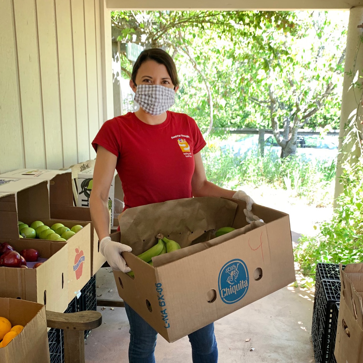 A woman, wearing a face mask and gloves, handles produce in cardboard boxes.