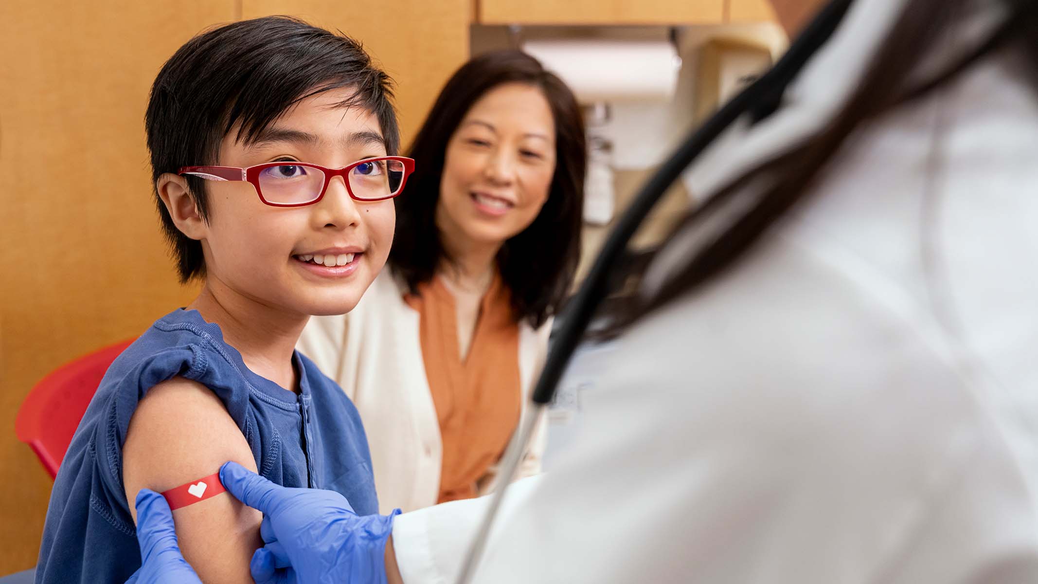 A CVS MinuteClinic practitioner applies a red bandage to a boy's arm after administering an immunization.