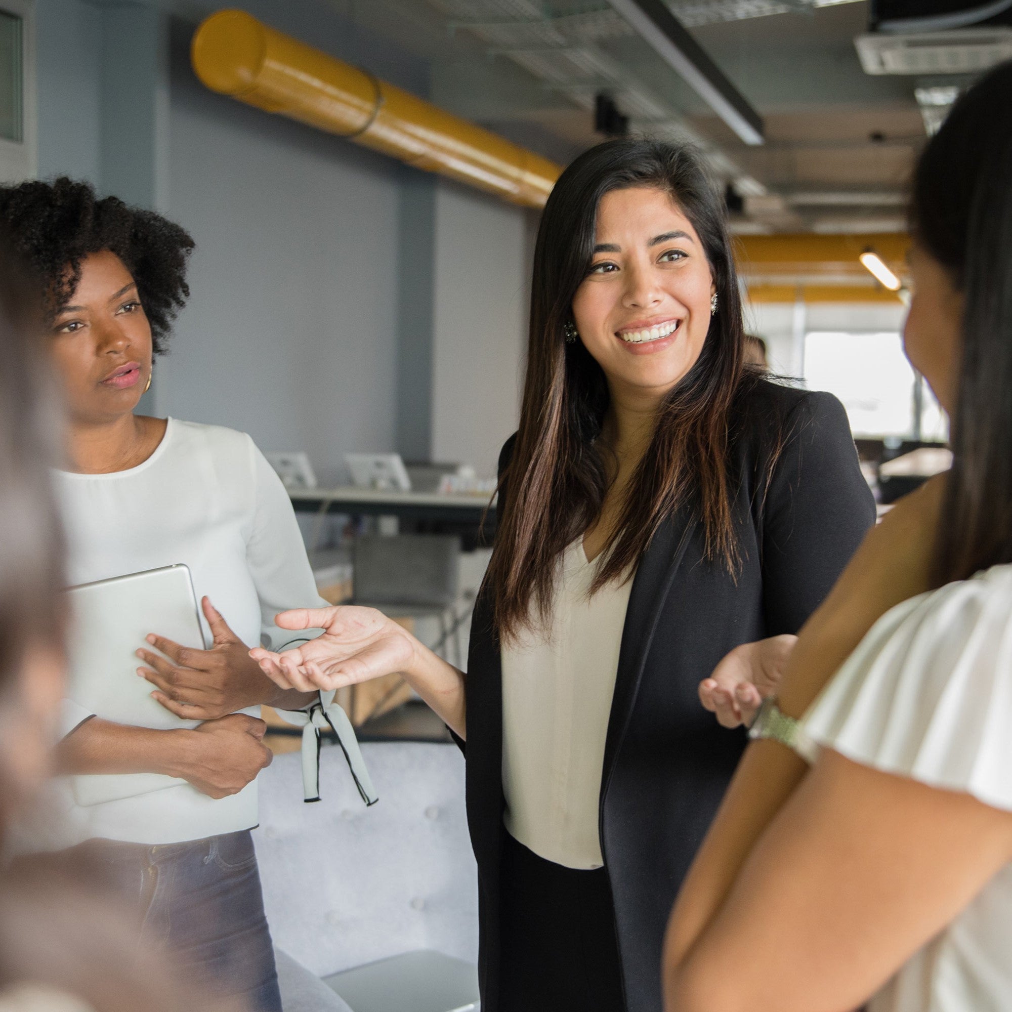 A group of female colleagues having a discussion in a very industrial, modern-looking meeting room.