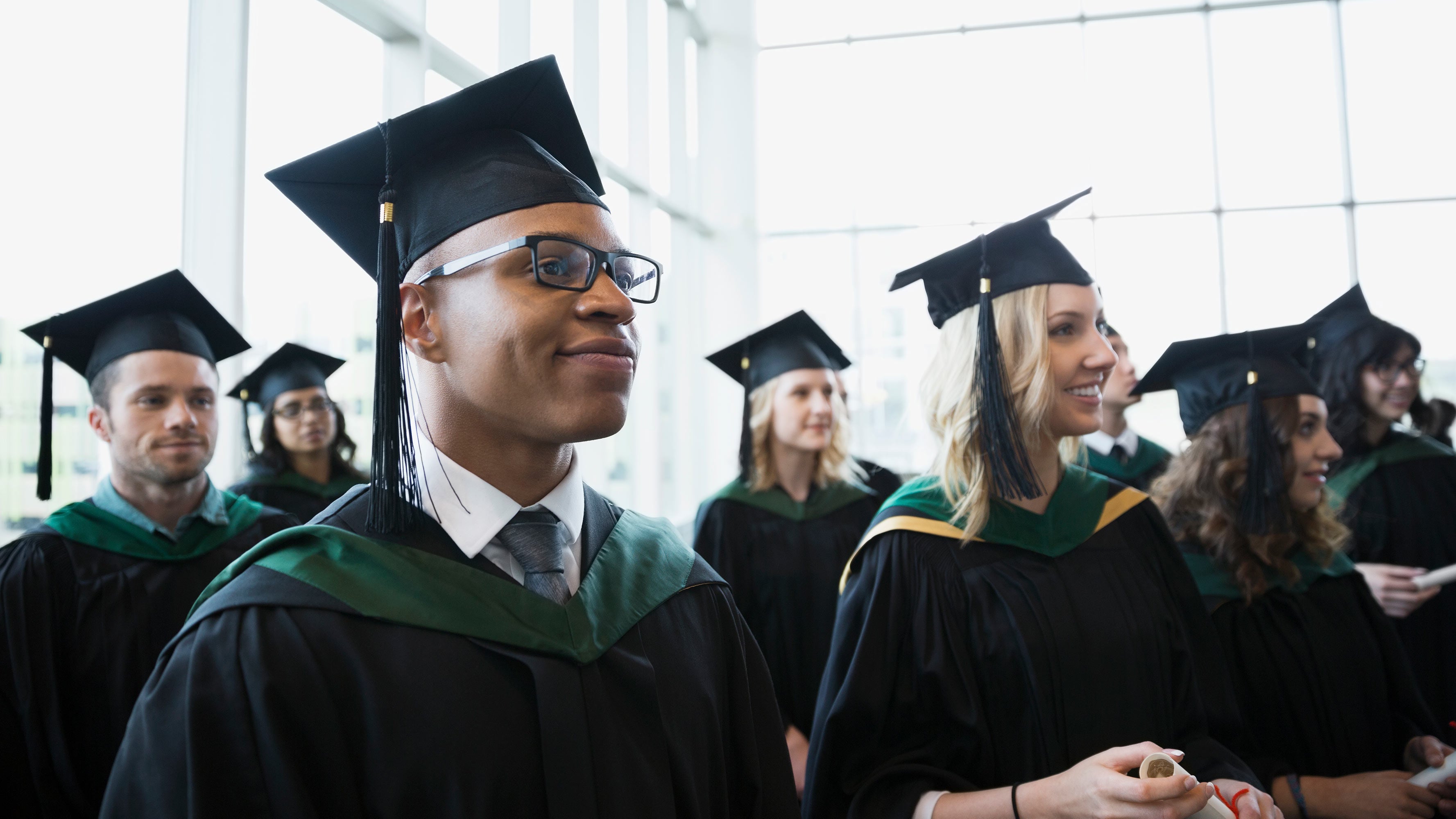A group of various students in a school auditorium, wearing graduation caps and robes.