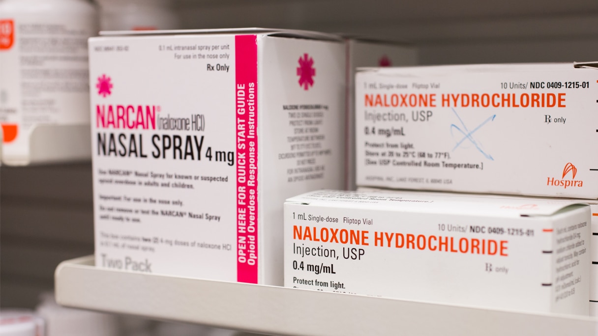 A pharmacy shelf displaying boxes of naloxone nasal spray.