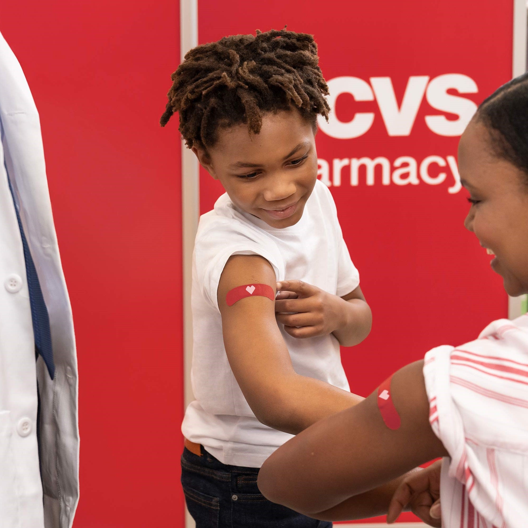 A young boy shows his upper arm bandaid to an adult with a matching bandaid.