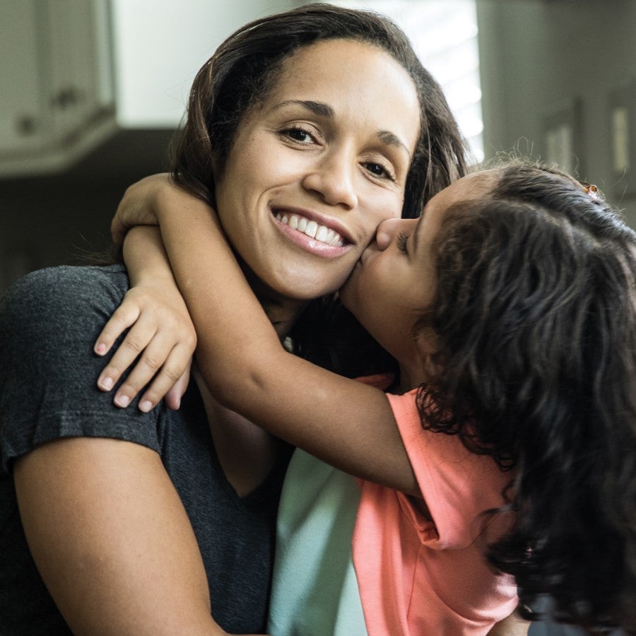 A mother smiles as she gets a kiss on the cheek from her daughter.