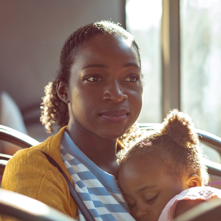 A woman rides the bus with her daughter sleeping on her lap.