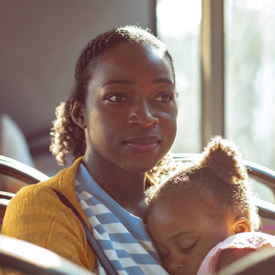 A woman rides the bus with her daughter sleeping on her lap.
