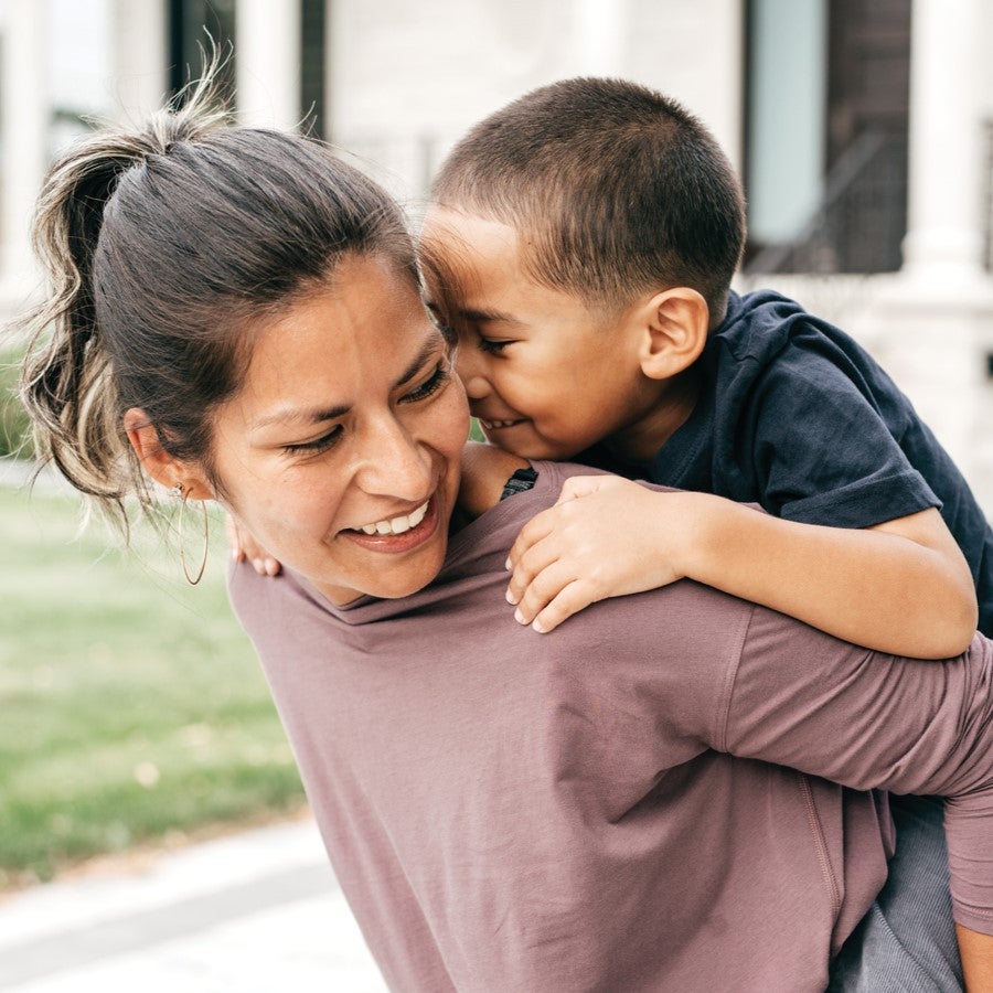 A son rides on his mom's back outside of their home.