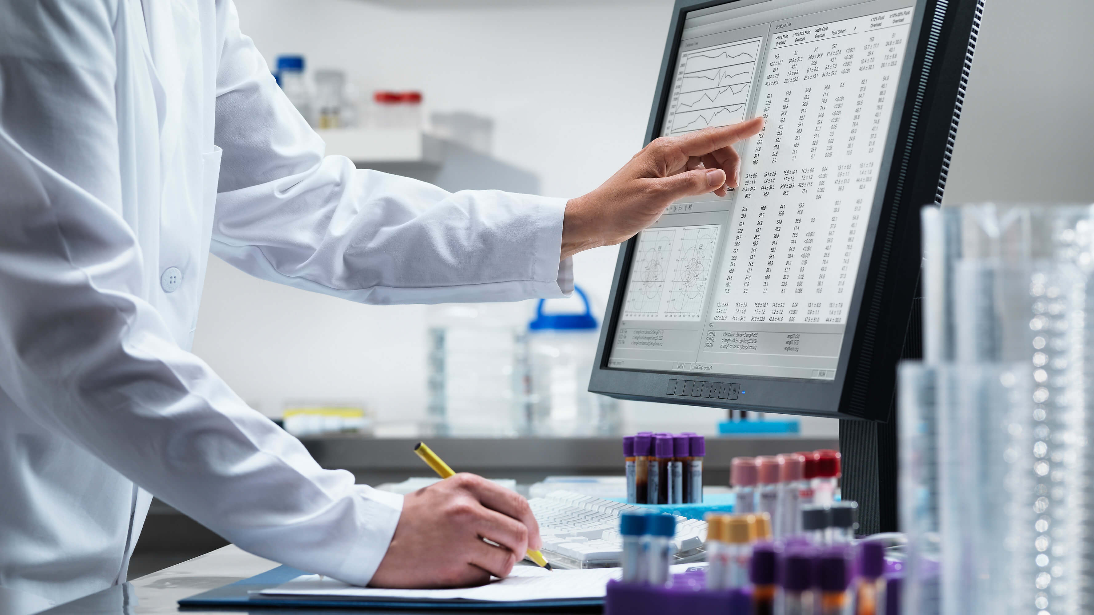 A lab technician in a laboratory records results from a computer screen displaying data.