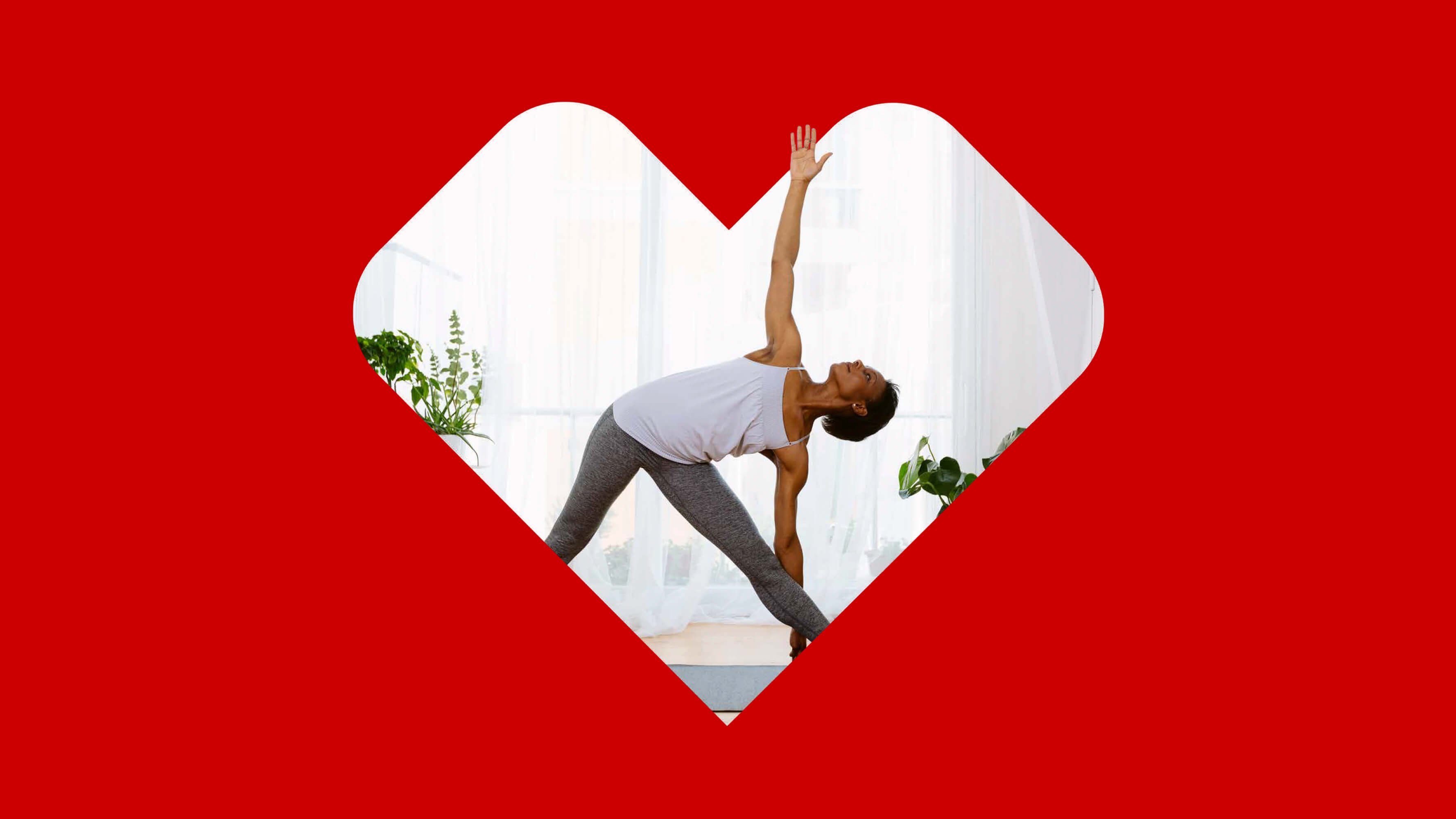 A woman in gray athletic clothes stretches and practices yoga poses in a very light and bright room. The photo is set inside of a CVS Health® heart on a red background.