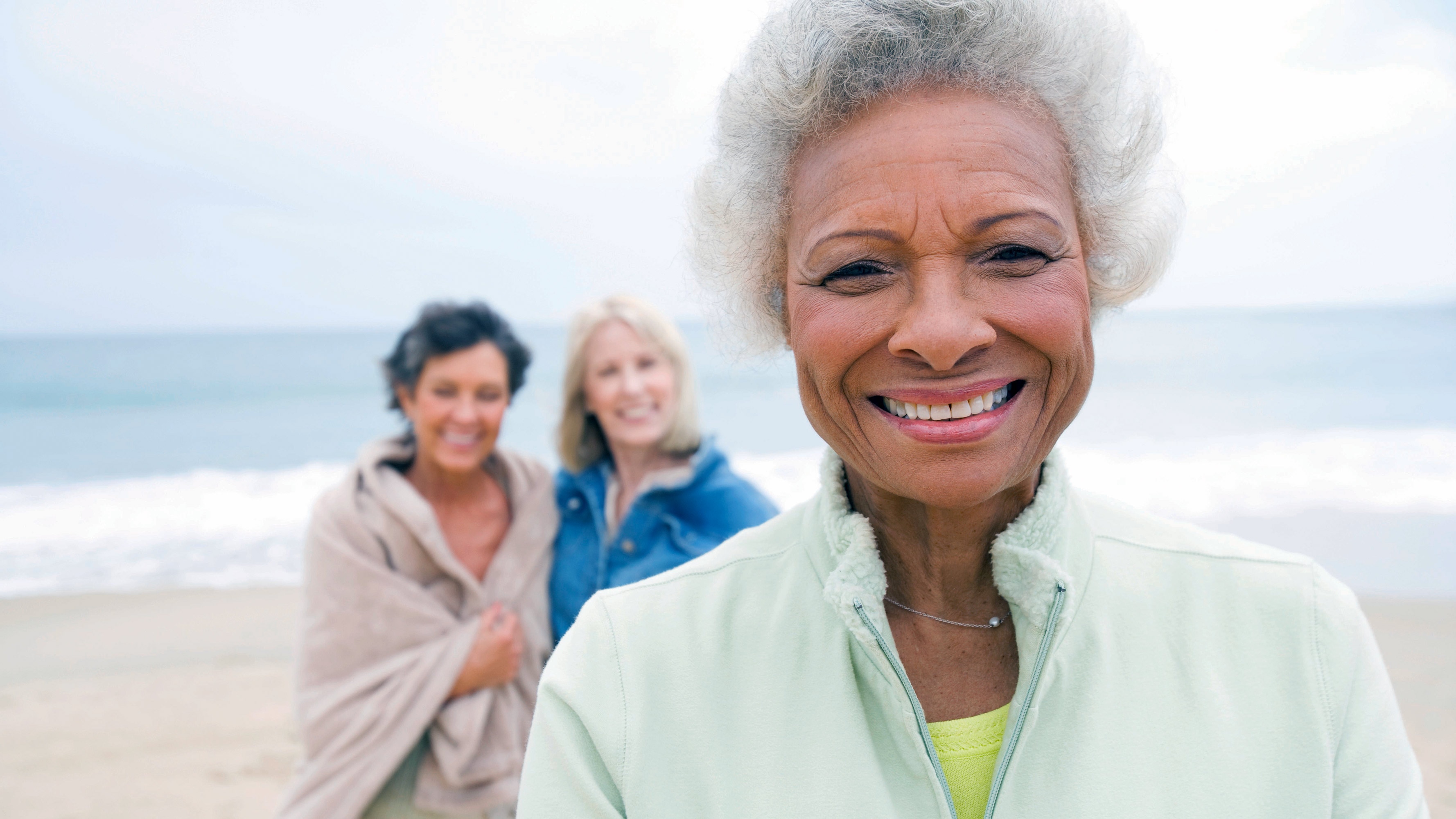 An older woman smiles while relaxing at the beach with two female friends.