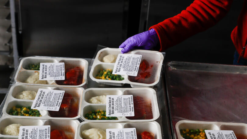 A volunteer arranges pre-packaged cooked meals, in sealed containers, on a tray for distribution.