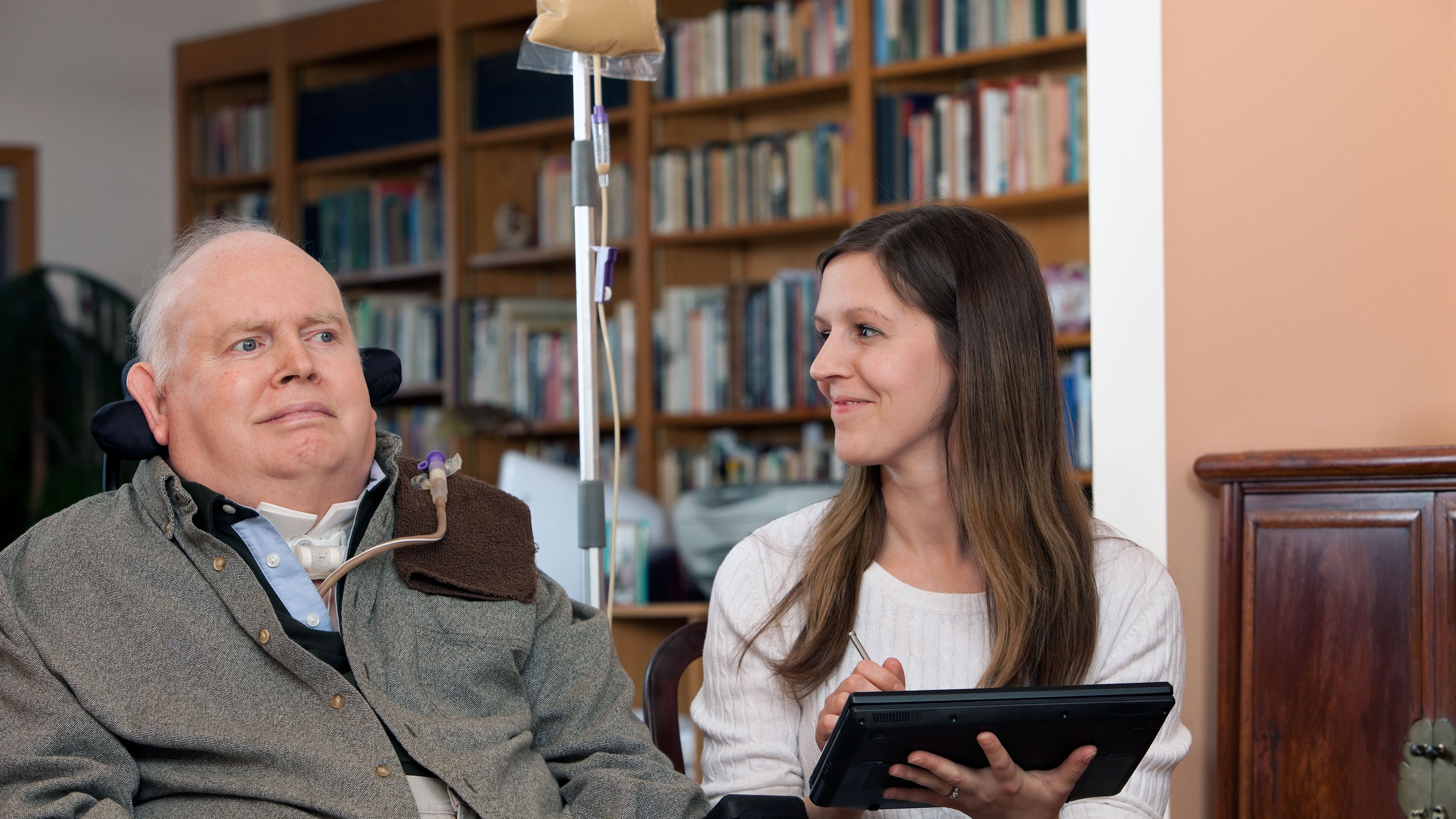 A practitioner, using a tablet computer, assists a patient with tube feeding therapy.