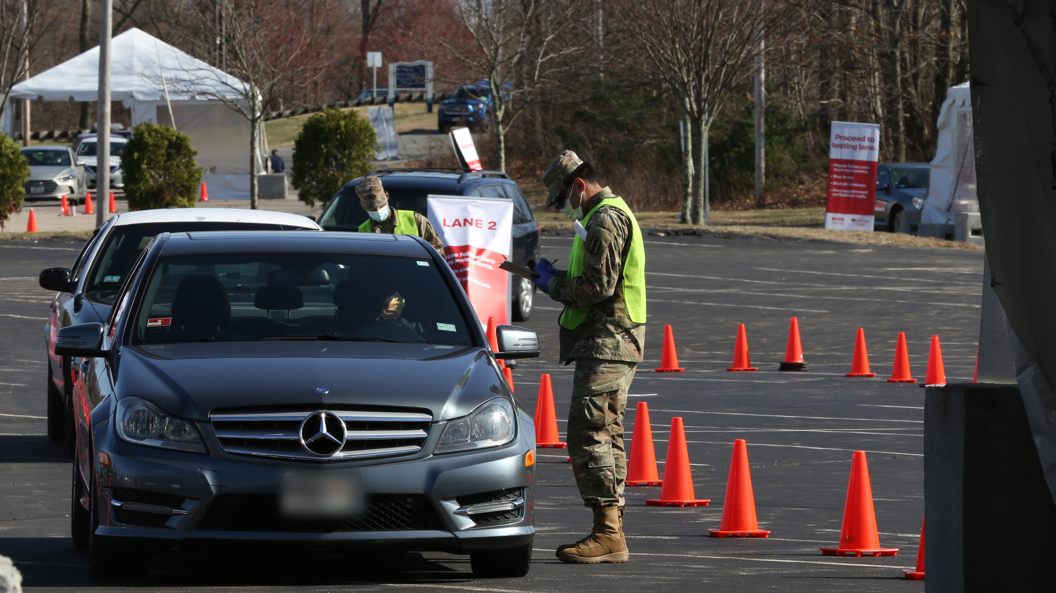 An Army National Guard member wearing fatigues, a traffic vest and a medical-grade mask, directs a patient through the rapid COVID-19 testing site in Lincoln, Rhode Island.
