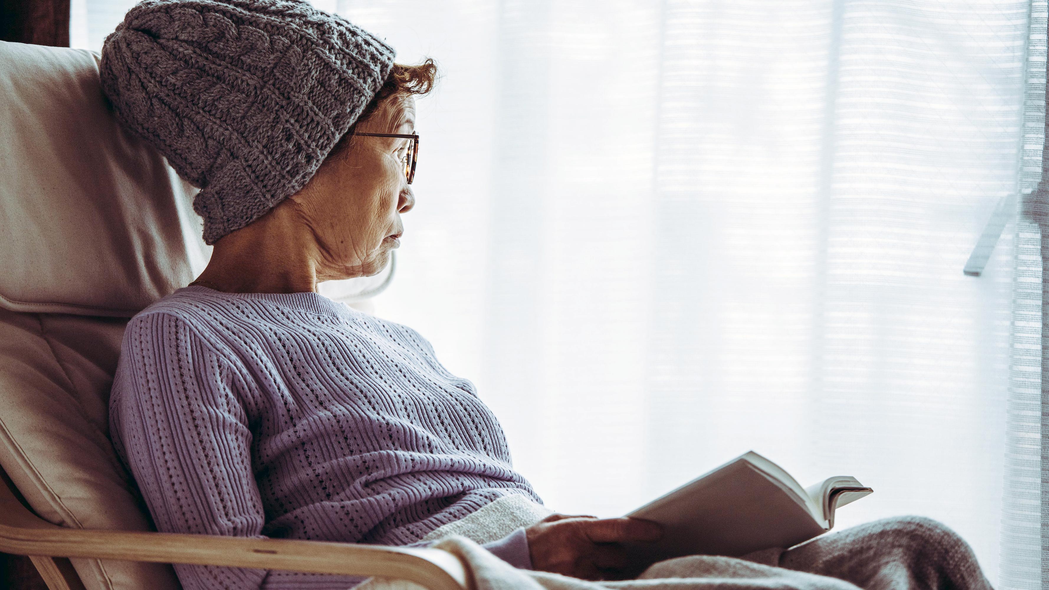 A photo of an older woman gazing out of a window with natural filtered light.