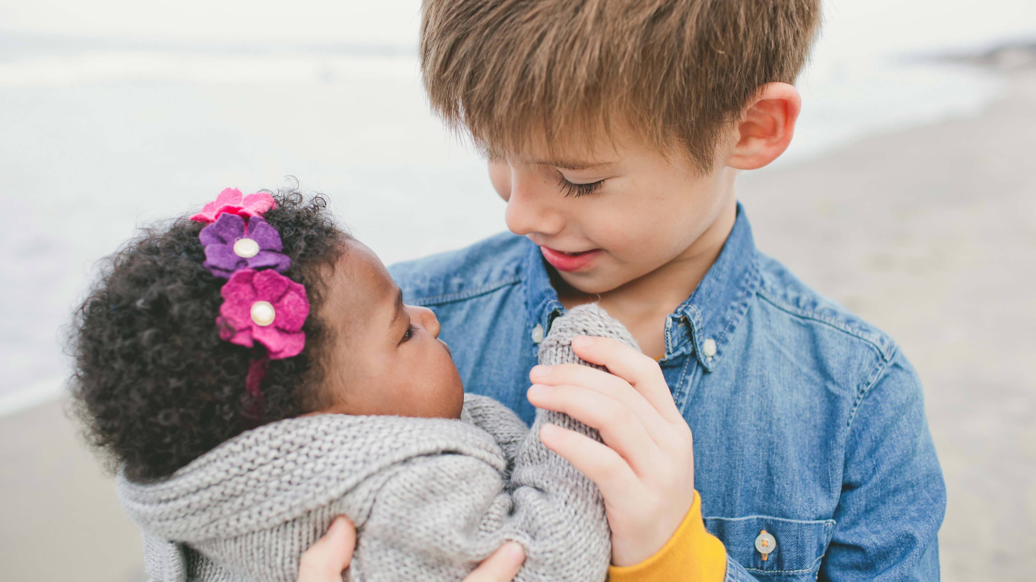 A young boy holds his adopted little sister in his arms looking at her face. 