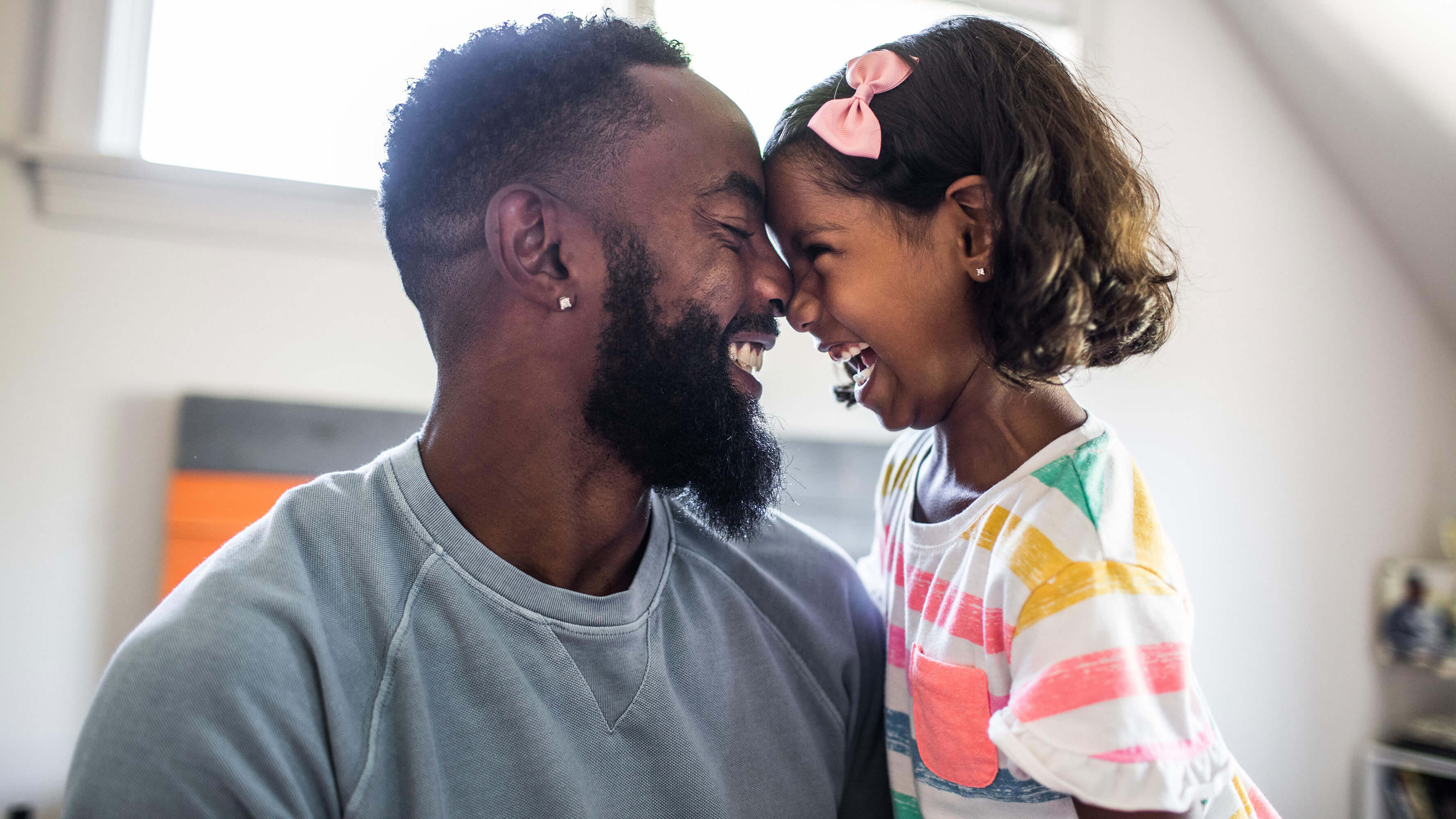 A father and daughter share in a smiling moment in a modern-looking living room.