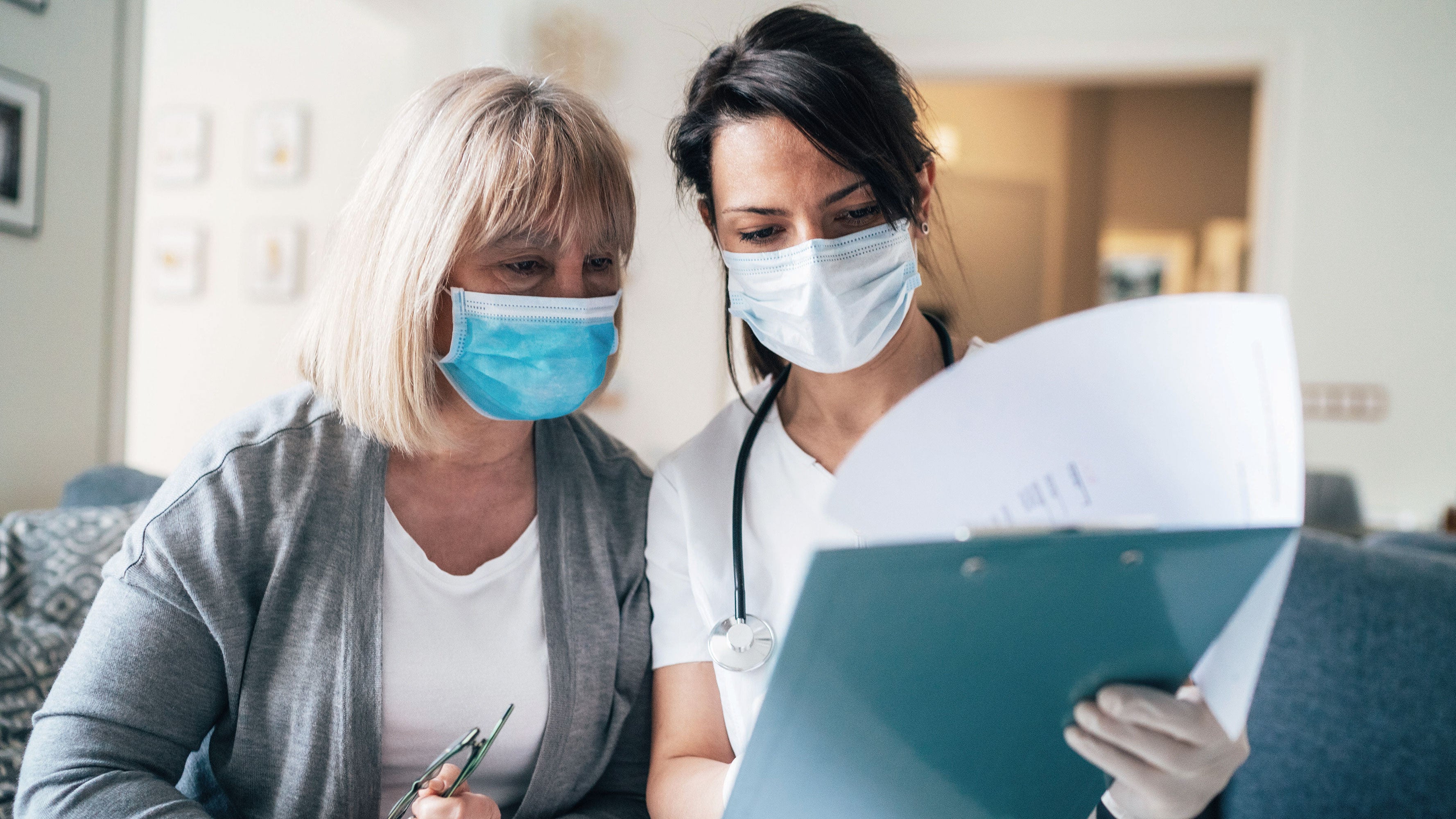 A nurse advises a patient in a medical facility, both wearing face masks.