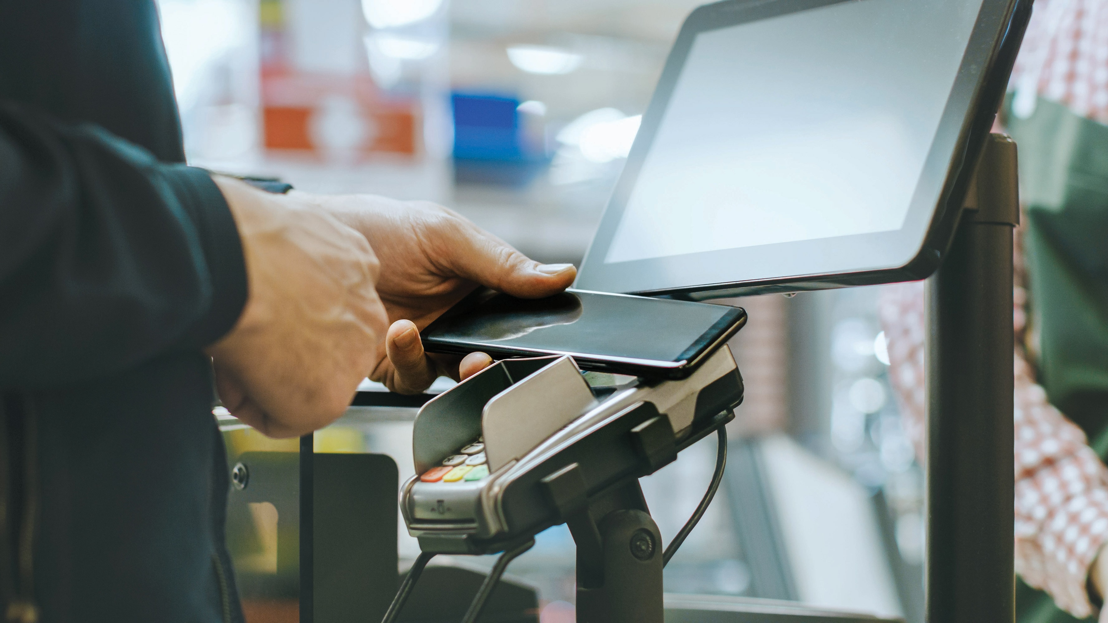 A person waves their smartphone over a credit card payment terminal to make a mobile payment at a checkout counter inside of a CVS Pharmacy store.