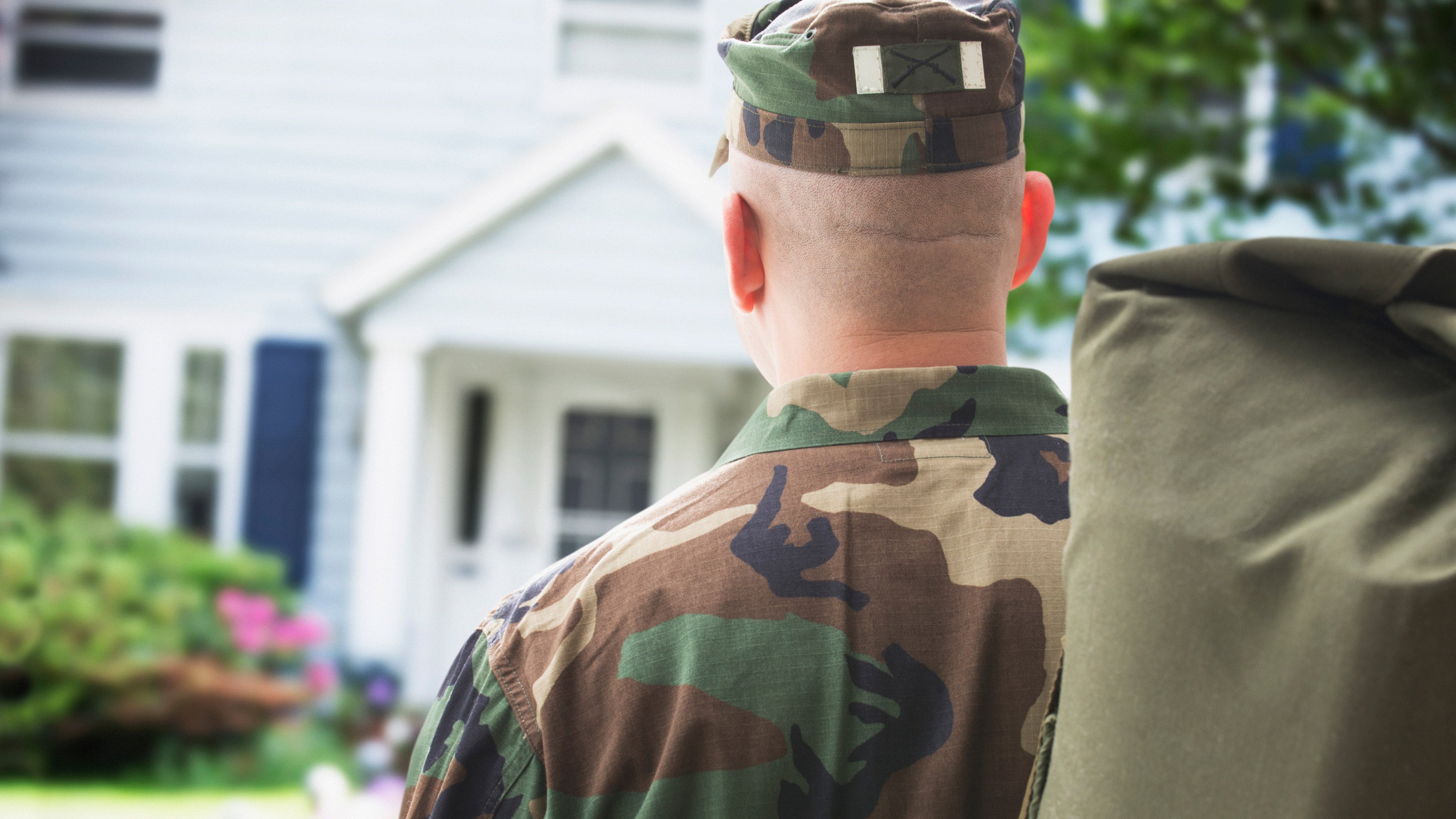 A soldier in military uniform walking toward his family home after returning from duty.