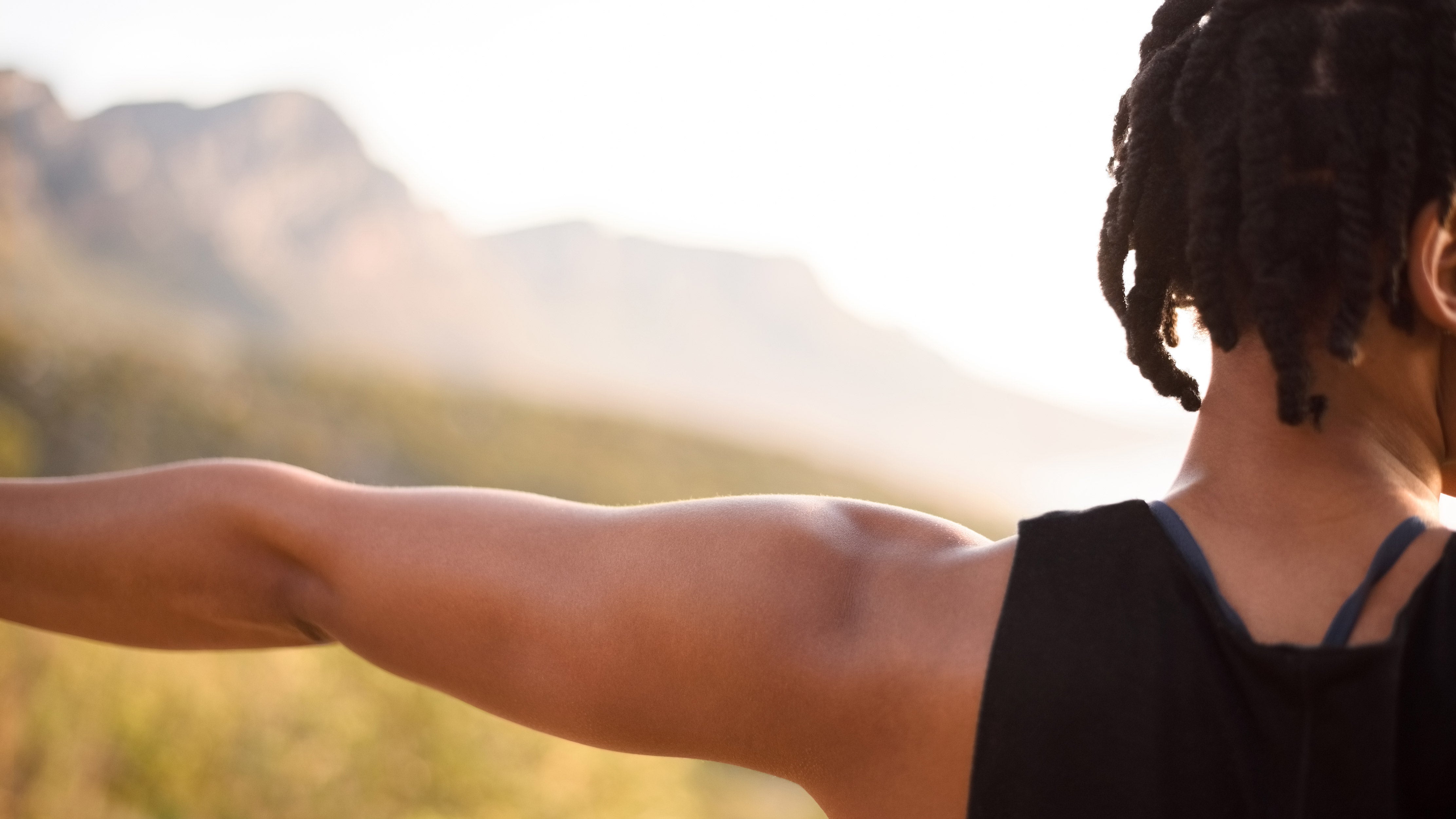 A young black woman practicing yoga outdoors with a mountain in the background. 