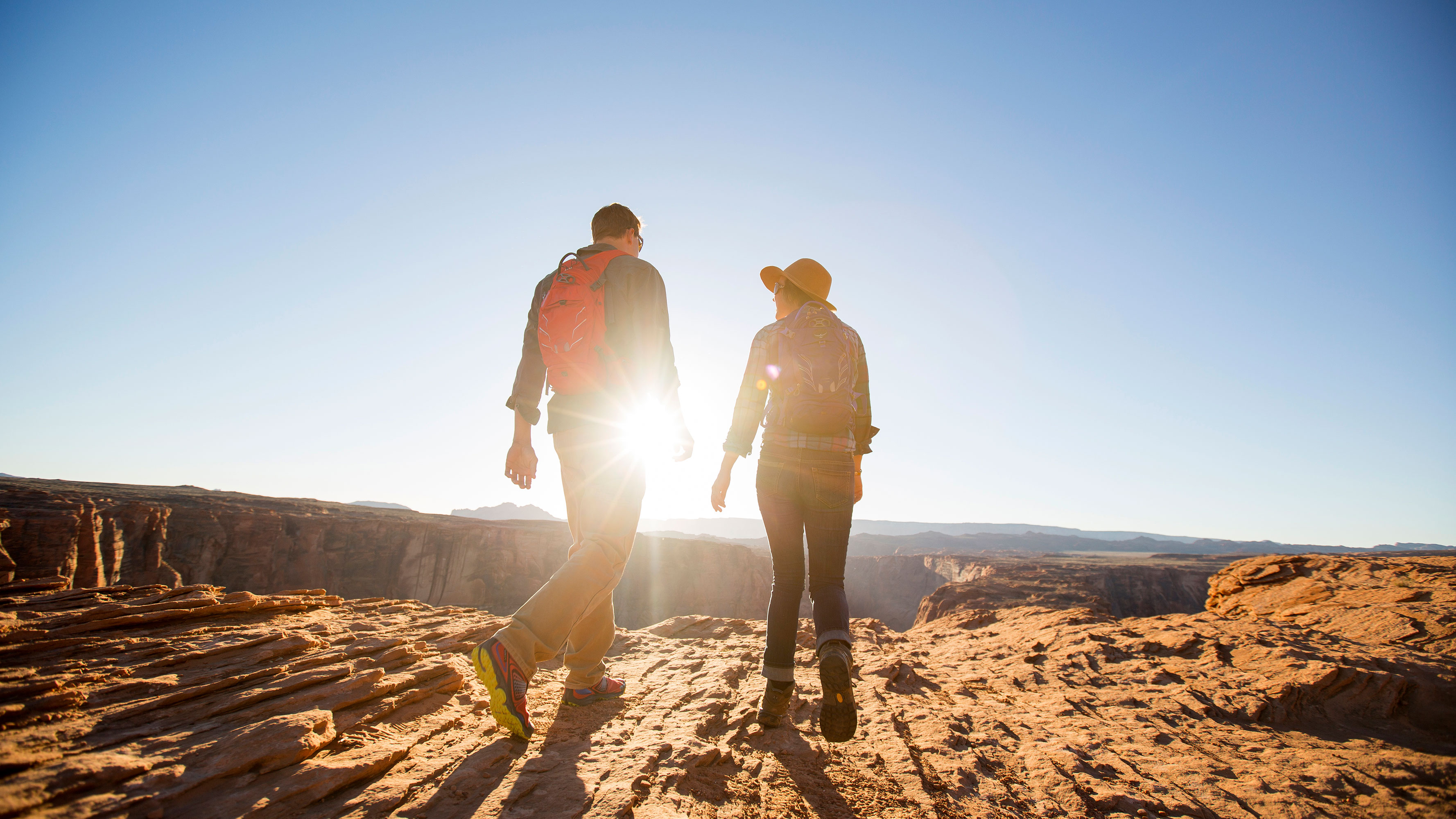A young couple hiking at the top of a canyon with the sun rising in front of them.