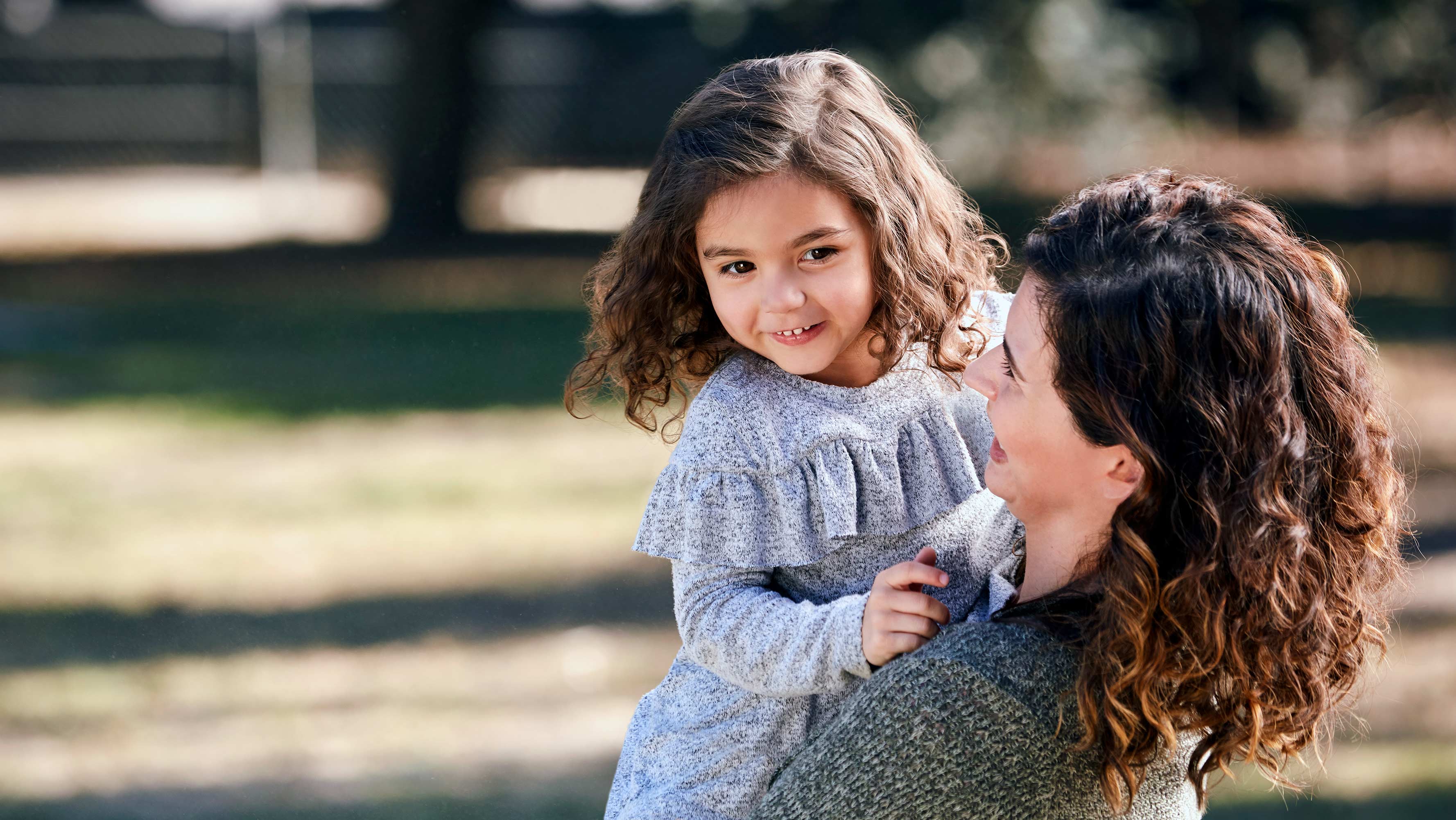 A mother holds her young daughter while playing in a city park.
