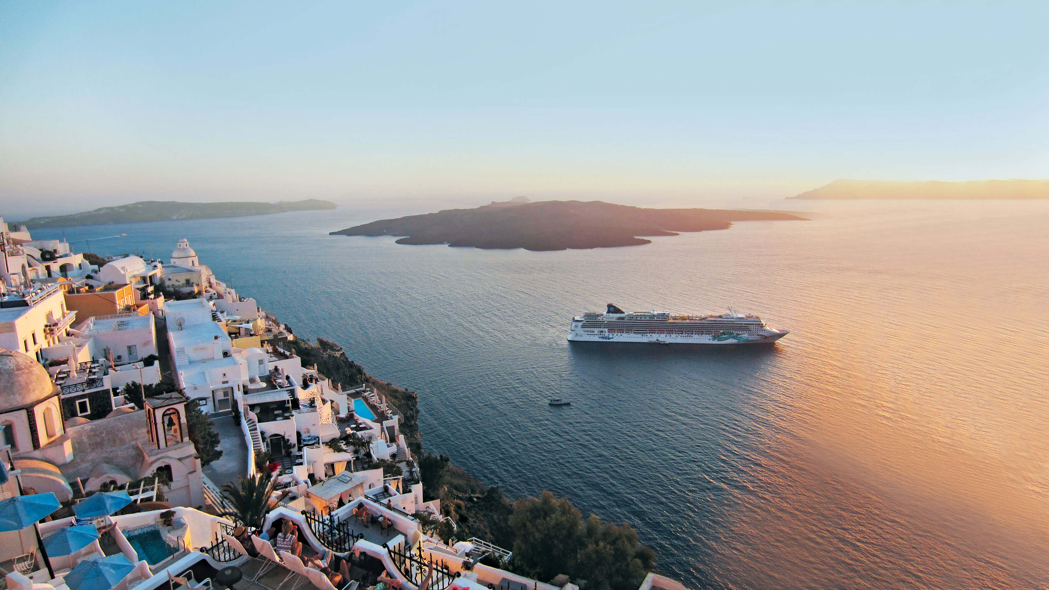 A cruise ship is seen anchored in a harbour, near the shore of a Mediterranean-looking village.