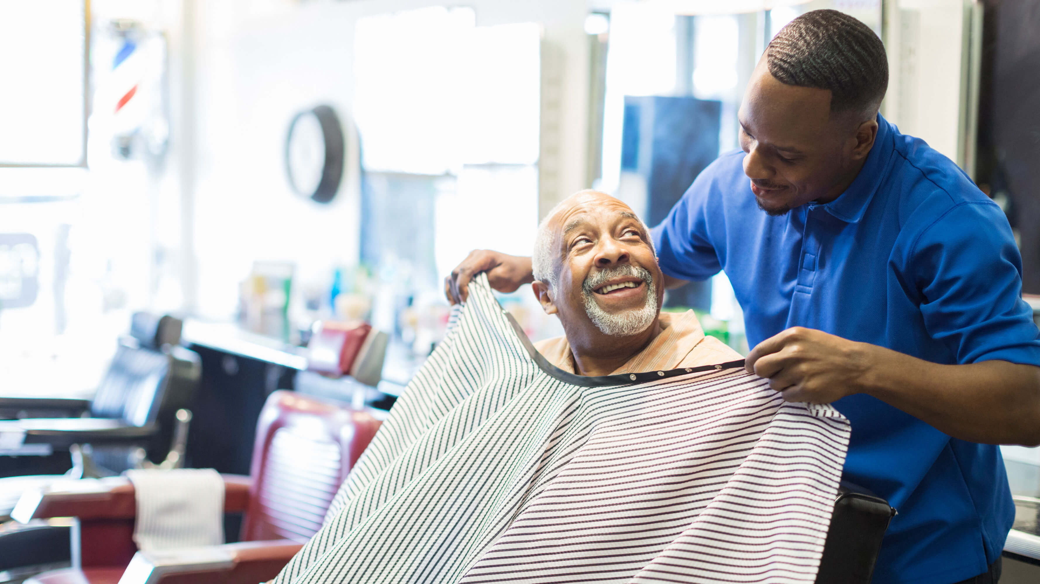A barber puts the cape on a a customer.