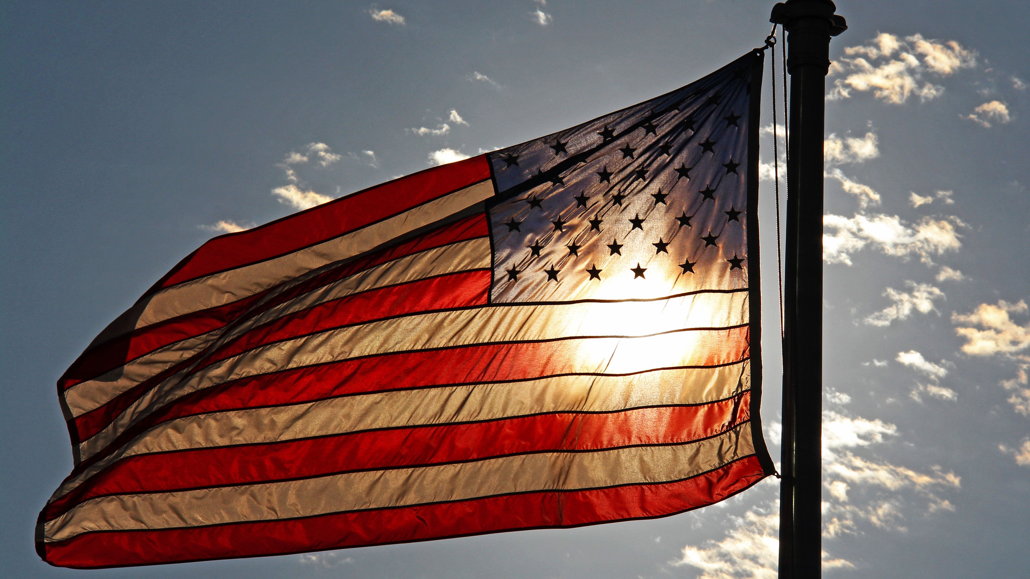An American flag waving in the wind in front of the sun.
