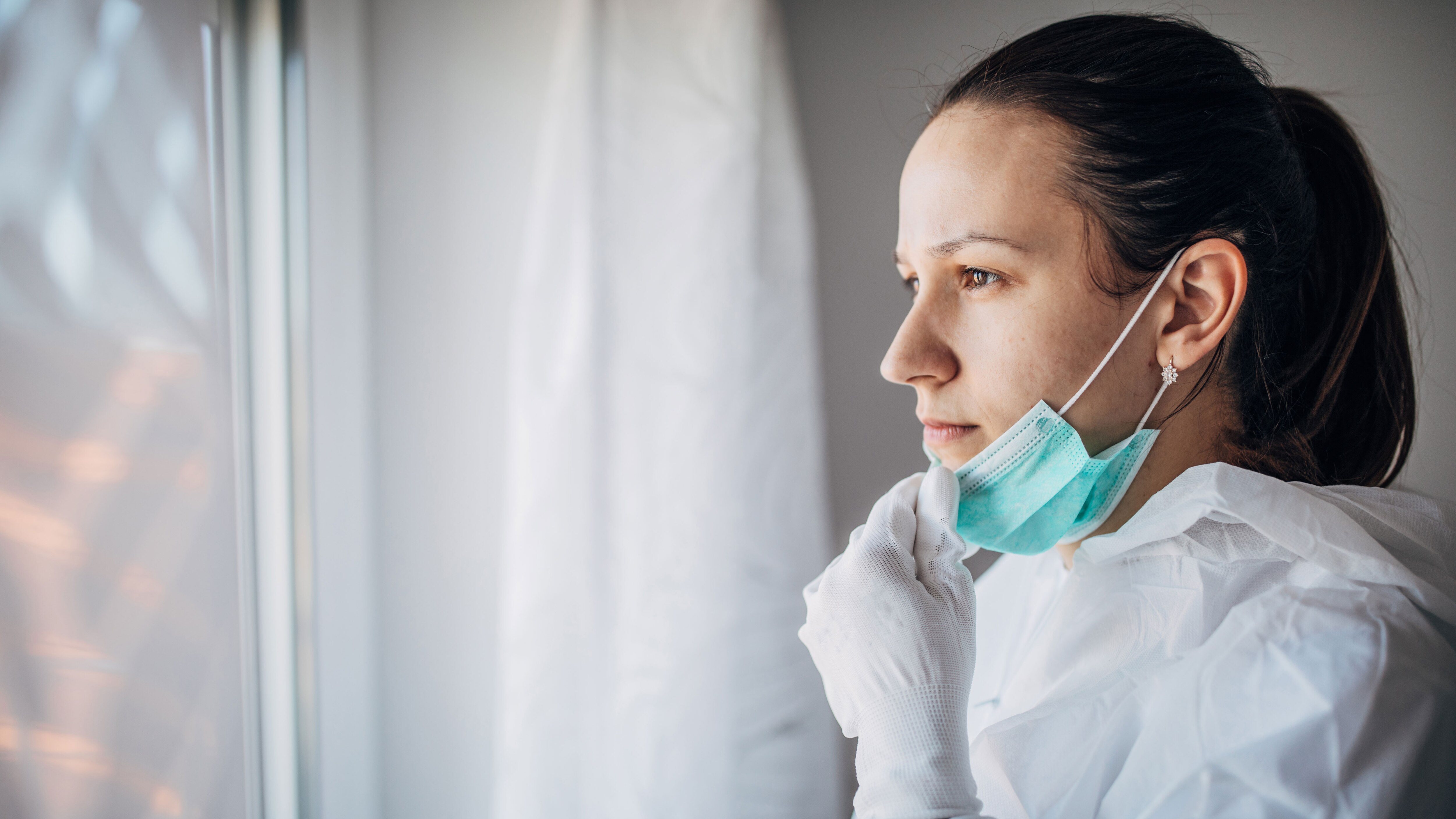 A health care worker, wearing PPE, stares out the window.