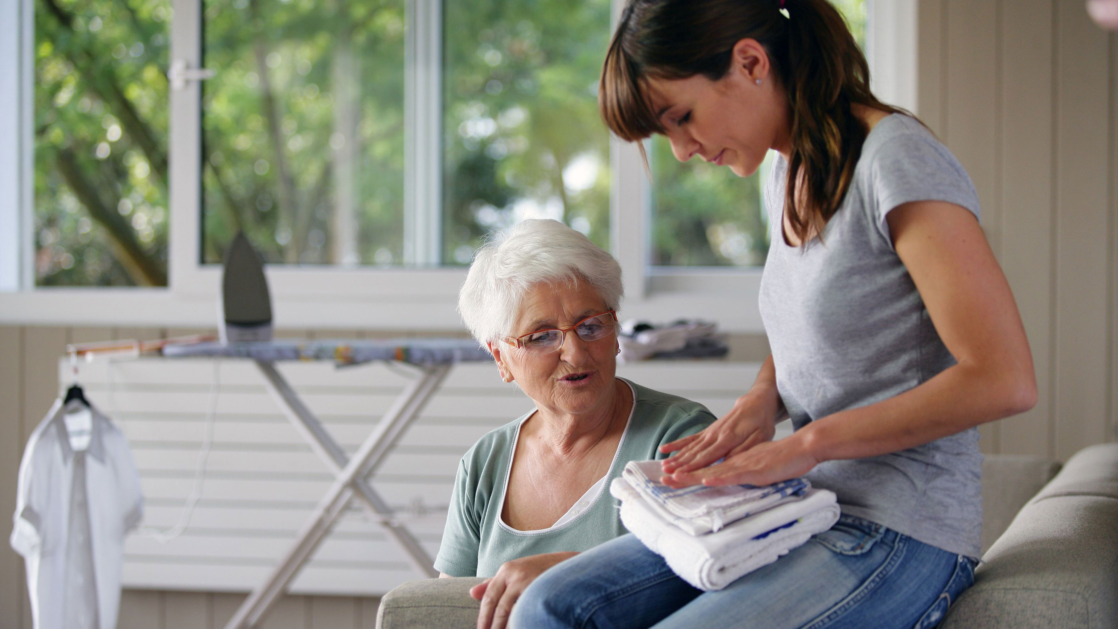 An elderly woman chats with a young woman folding towels.