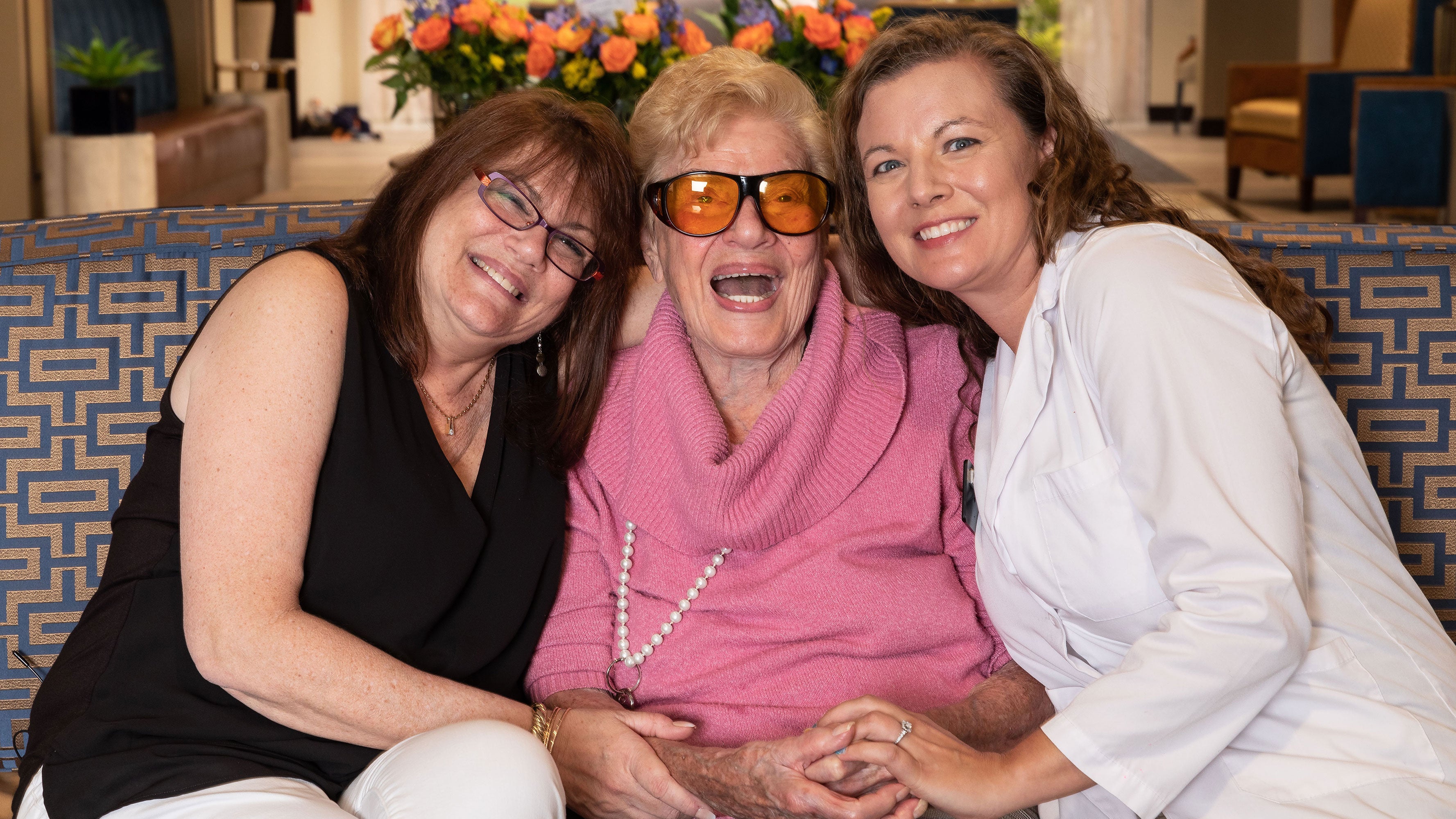 Three women huddle close to each other on a couch to smile and pose.