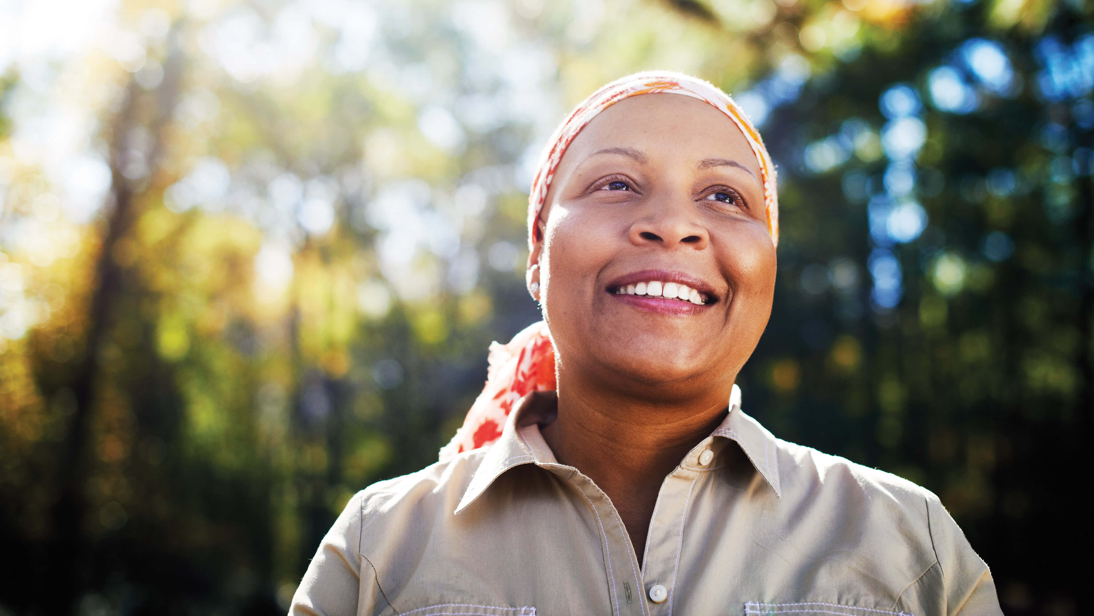 A woman wearing a scarf to cover her head stands outside near her trees at golden hour.