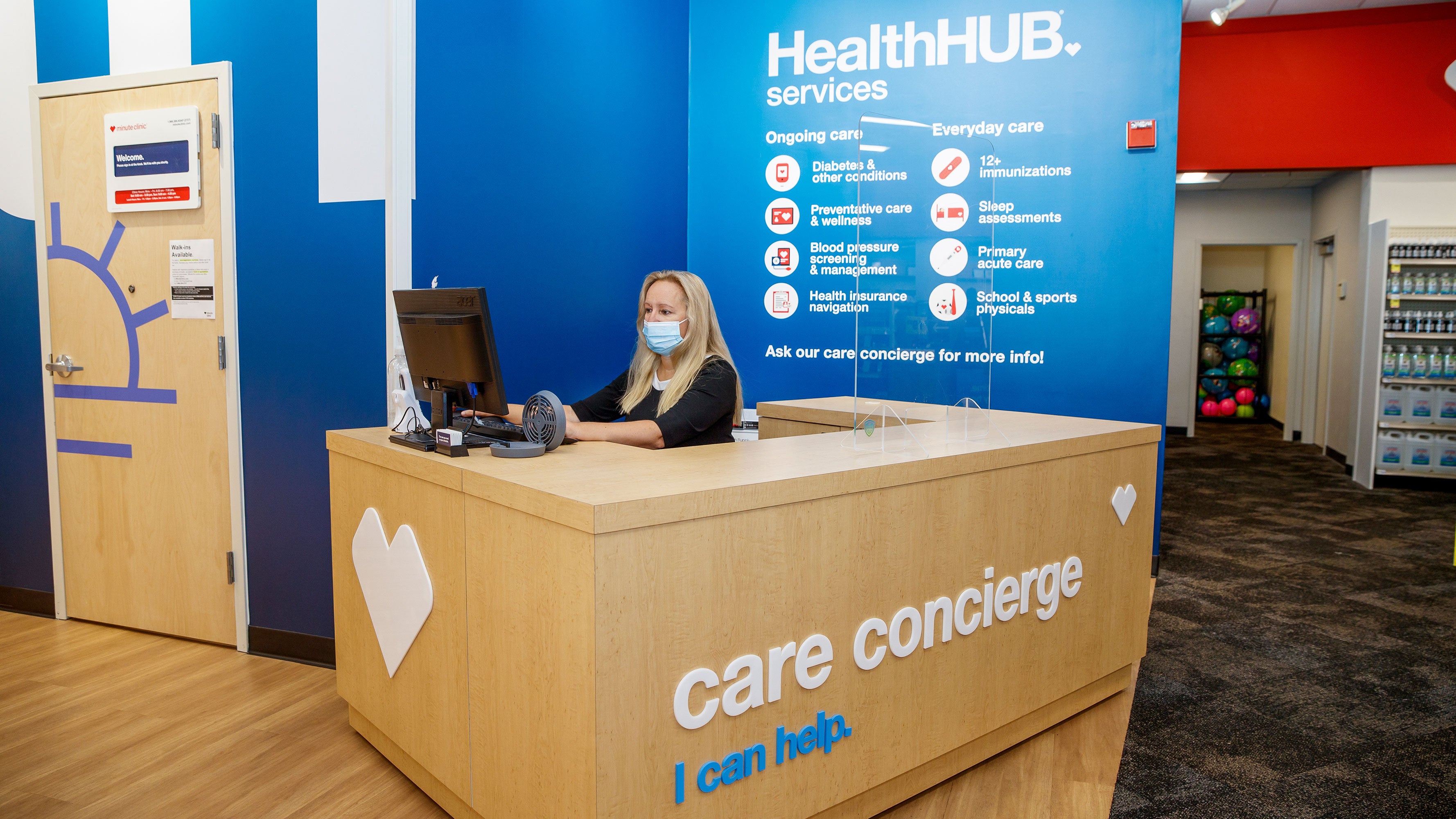 A masked Care concierge uses the computer at the check-in station for a HealthHUB inside a CVS MinuteClinic