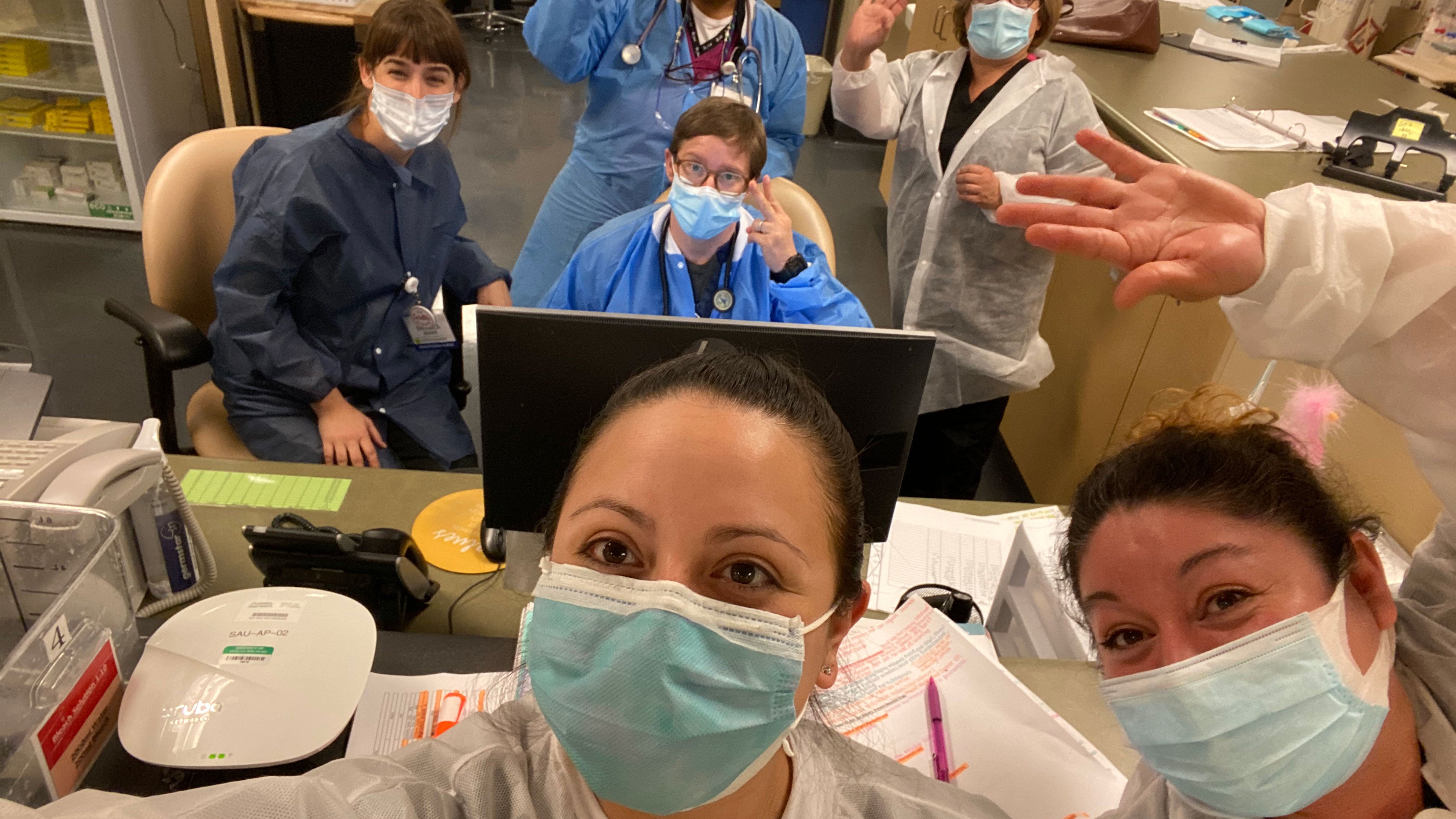 Masked nurses take a selfie at a nurses&#039; station.