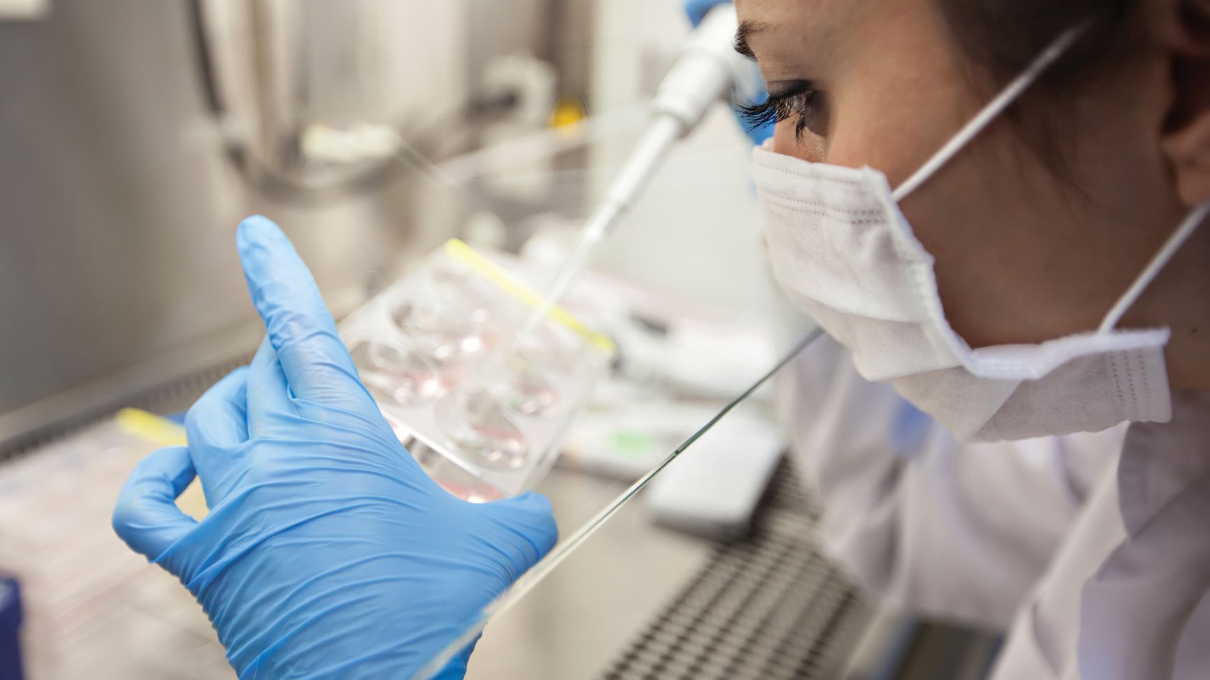 A masked lab technician wears gloves while piping a catalyst into tubes for results.