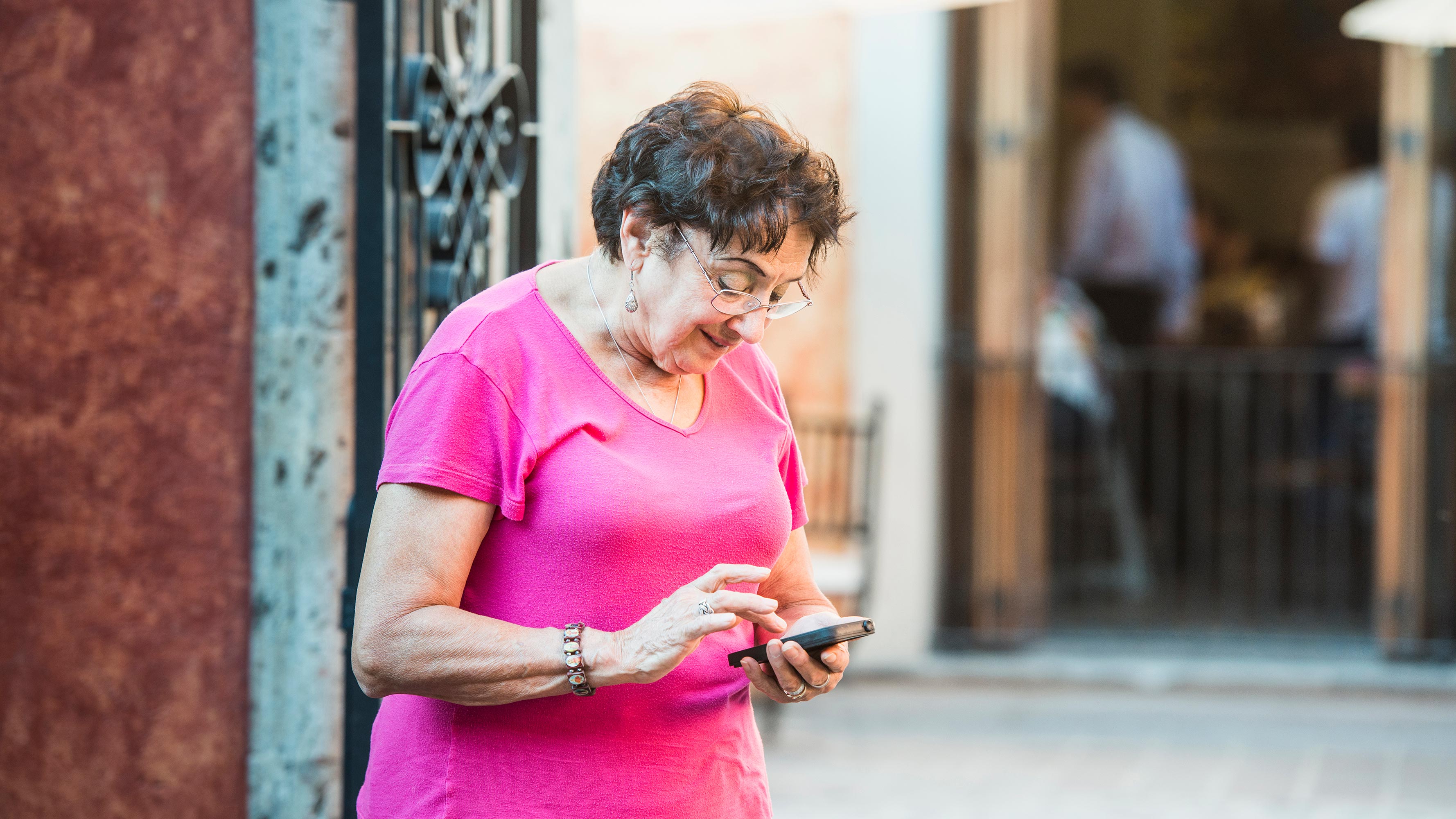 A middle-aged woman stands outside a restaurant to use her smart phone.