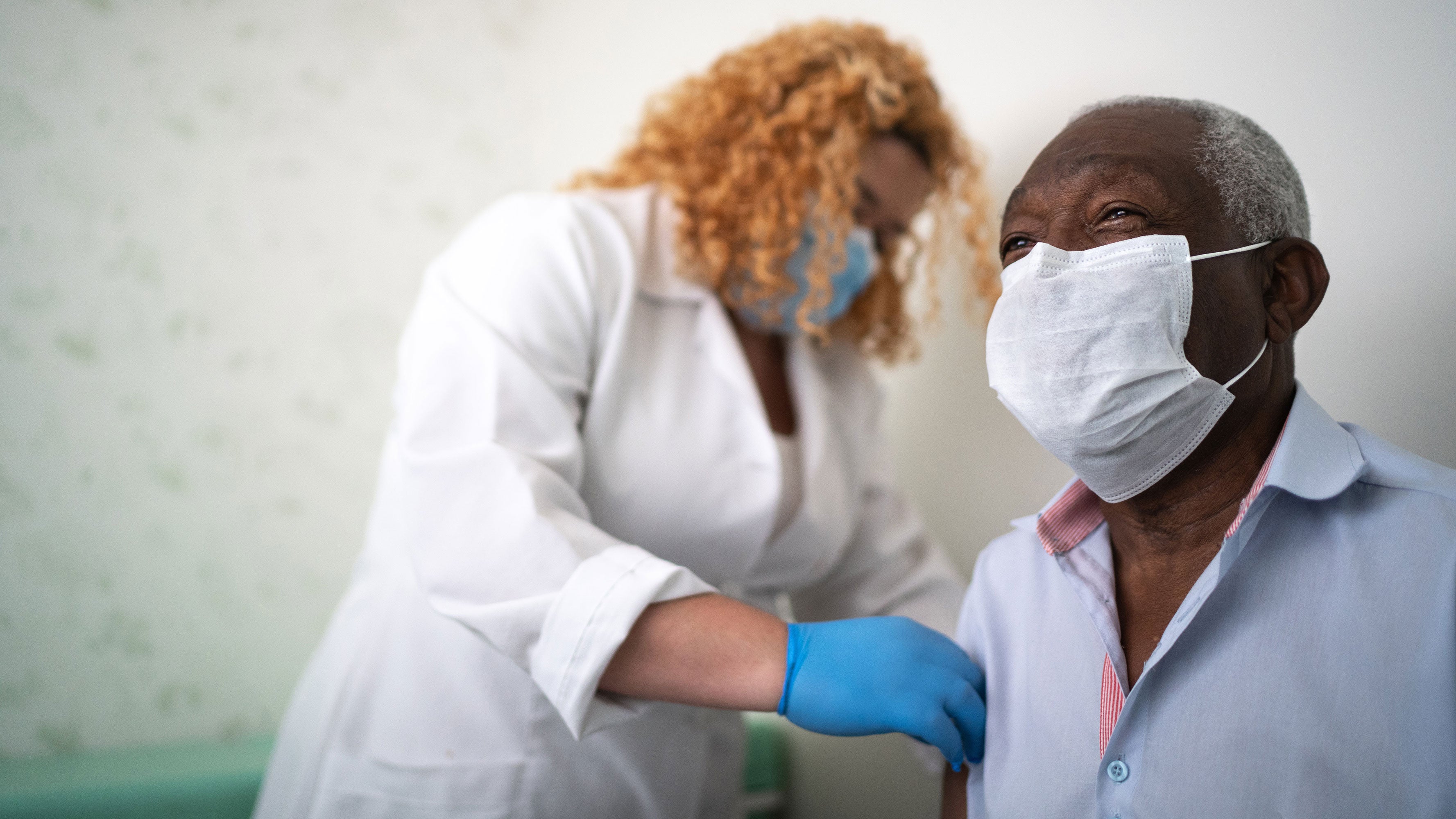 A nurse prepares a patient’s arm, both wearing face coverings, for a vaccination