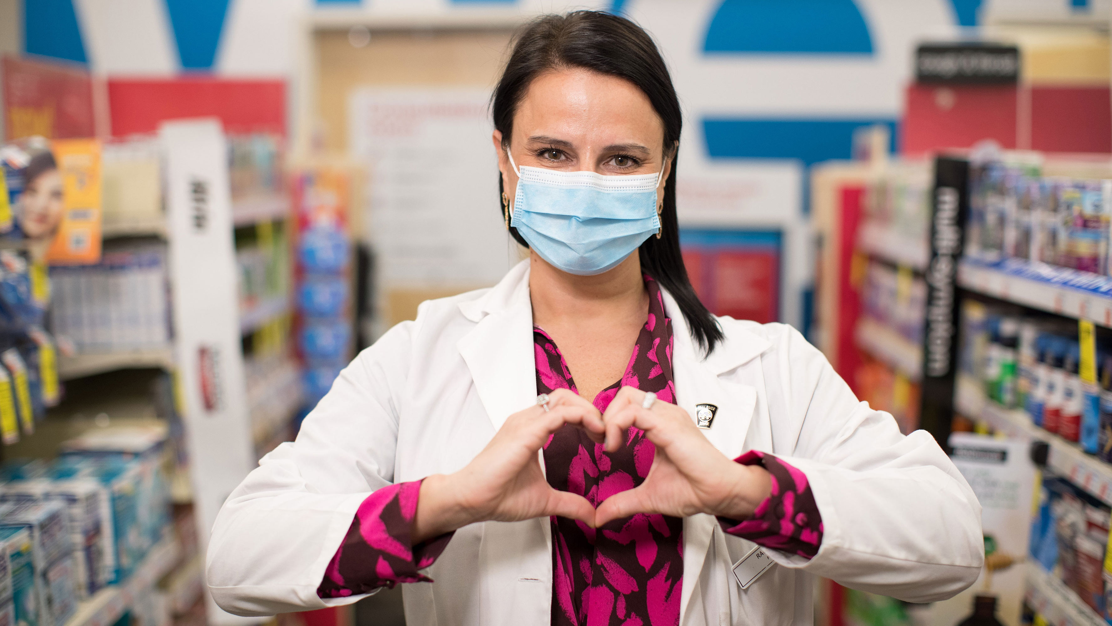 A CVS Pharmacy employee, wearing a face mask, makes a heart gesture with her hands as she stands in a CVS Pharmacy in Fall River, Massachusetts.
