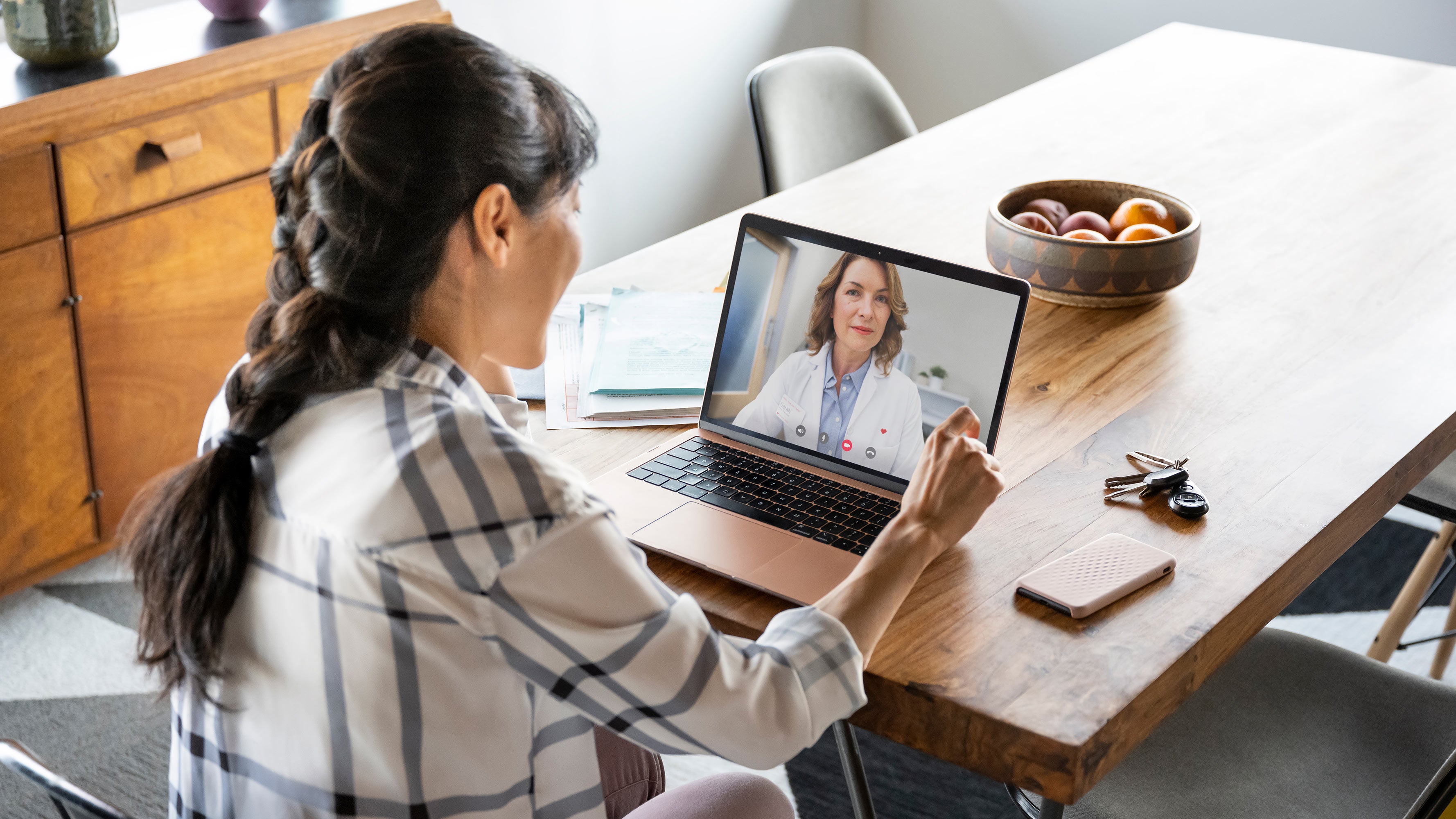 A female patient is seen in her kitchen, conferencing on a video chat with her health care provider.