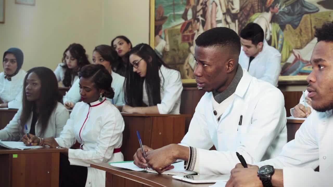 Students of color take notes while attending class in a lecture hall.