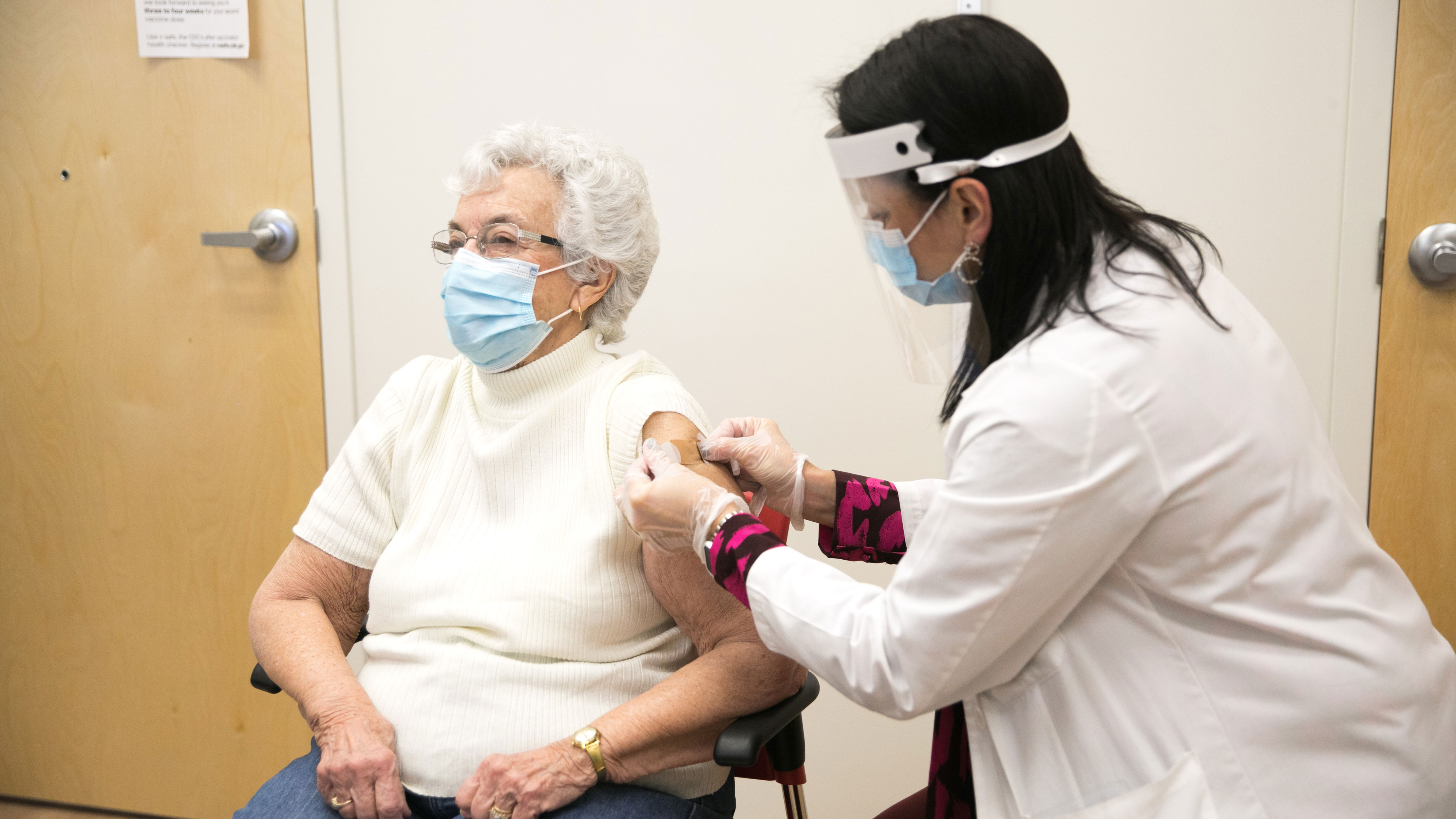 An elderly woman getting vaccinated by a pharmacy technician