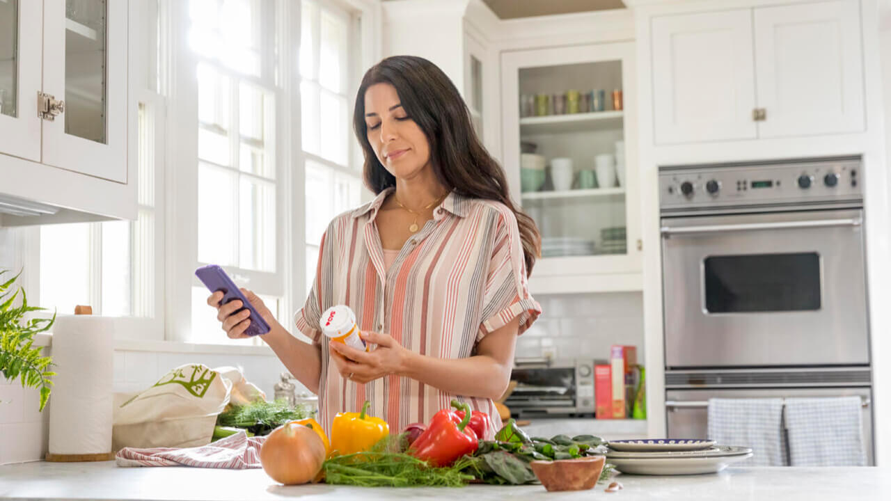 A woman standing at her home kitchen scanning a talking prescription bottle