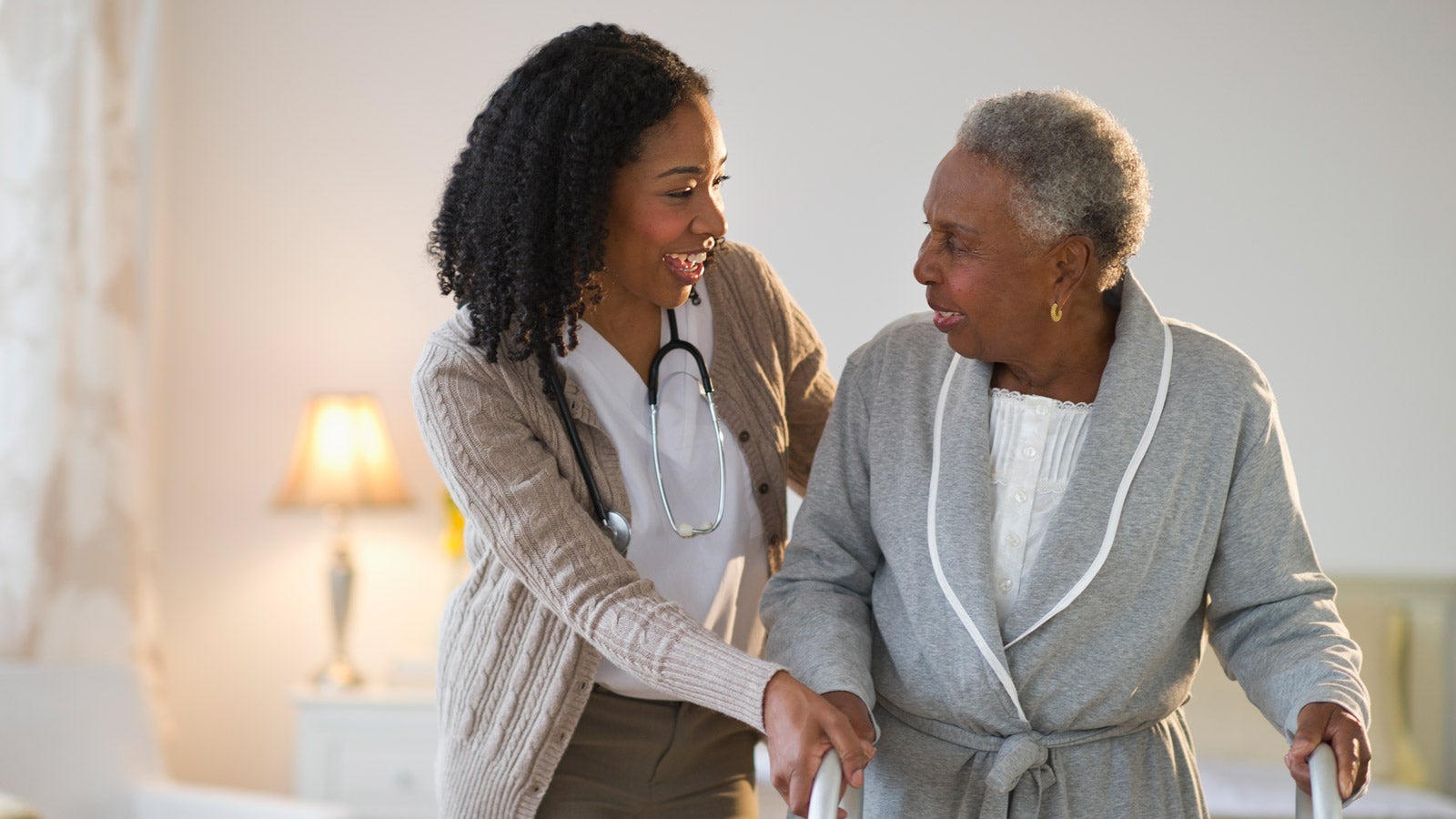 A healthcare provider walks with a senior patient using a walker.
