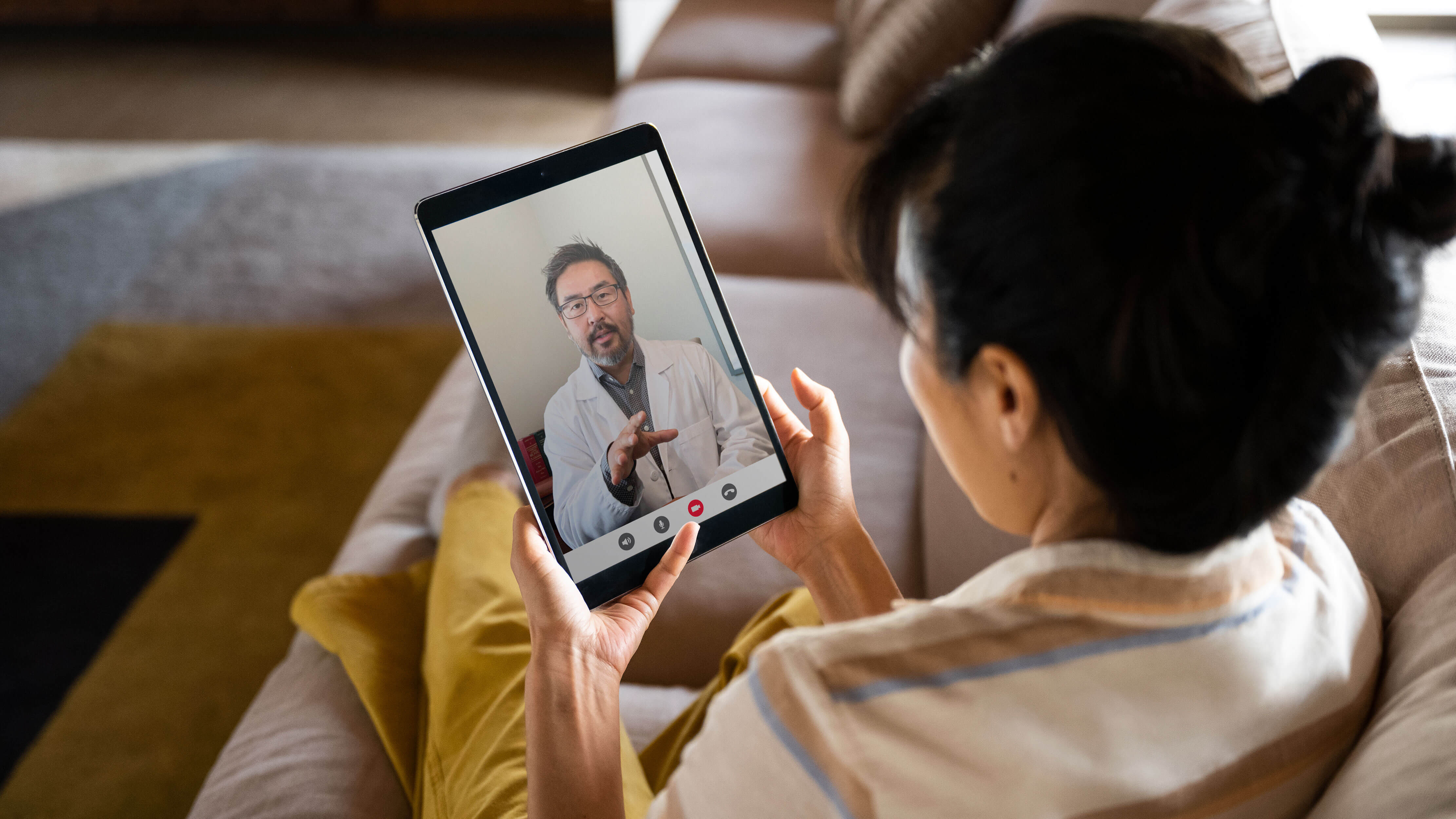 Woman sitting on couch talking to medical professional over tablet